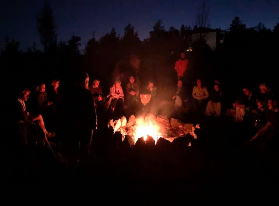 People sit in a circle around a campfire at night.
