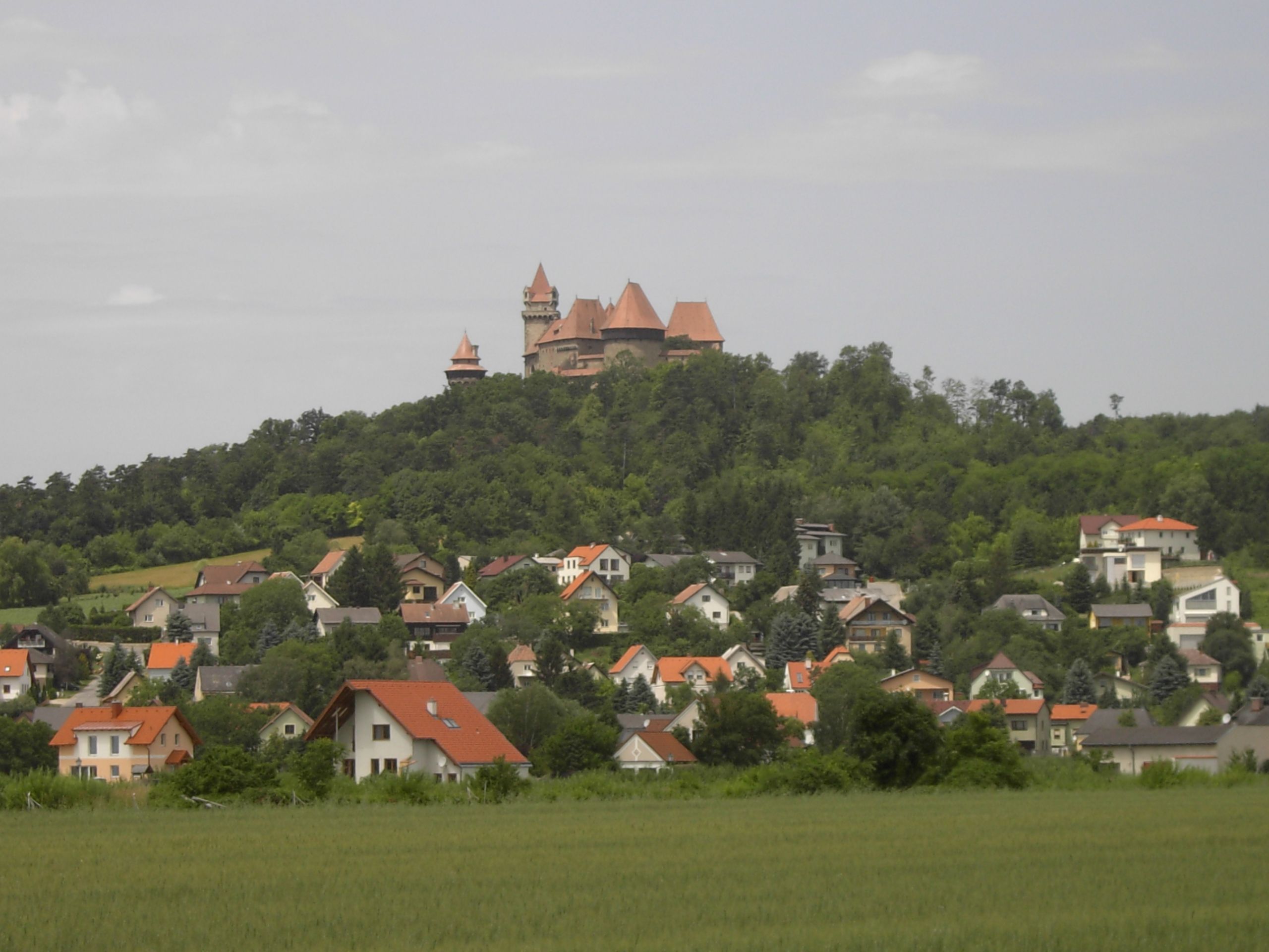 Kreuzenstein Castle sits on a hill above the village of Leobendorf, surrounded by green trees and houses.