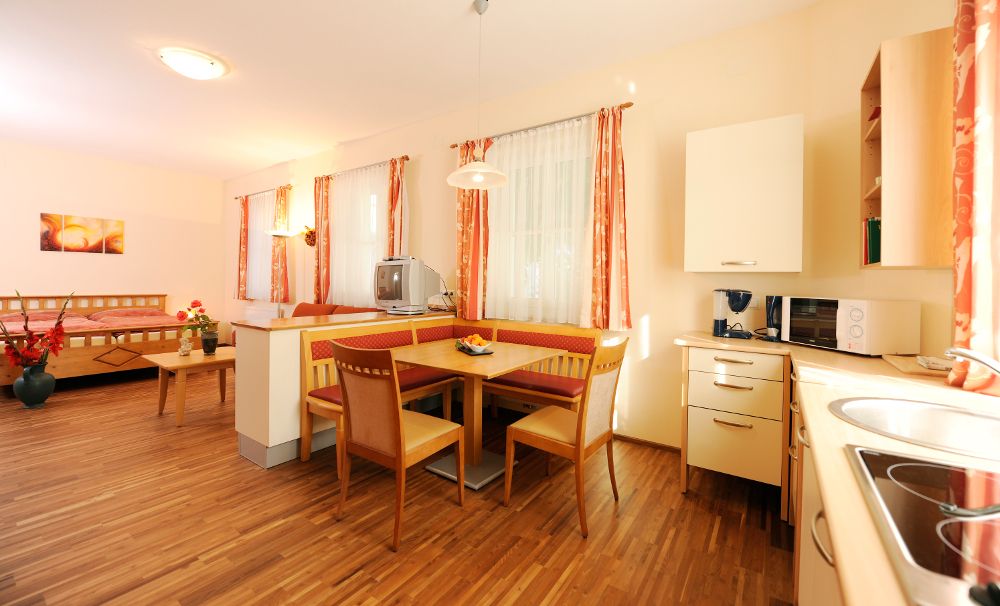 Bright room with wooden floor, dining table, kitchen and bed.