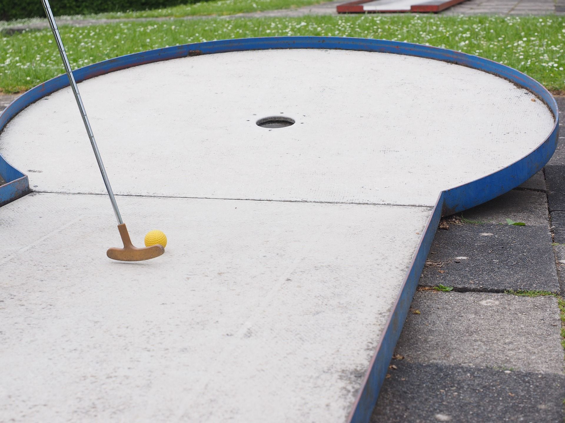 Minigolf course with club and yellow ball in front of a hole.