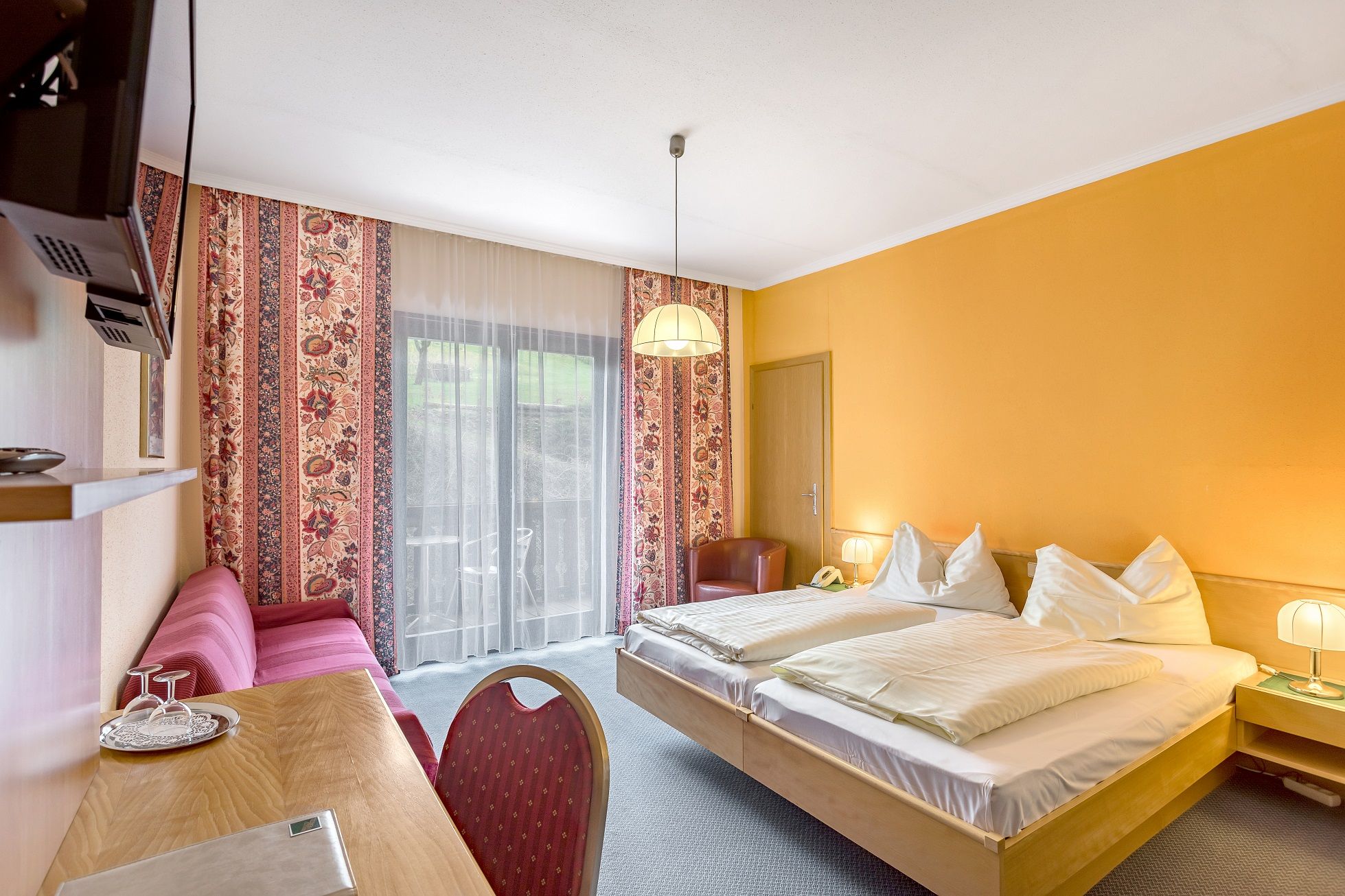 Hotel room with double bed, yellow walls, red sofa and balcony.