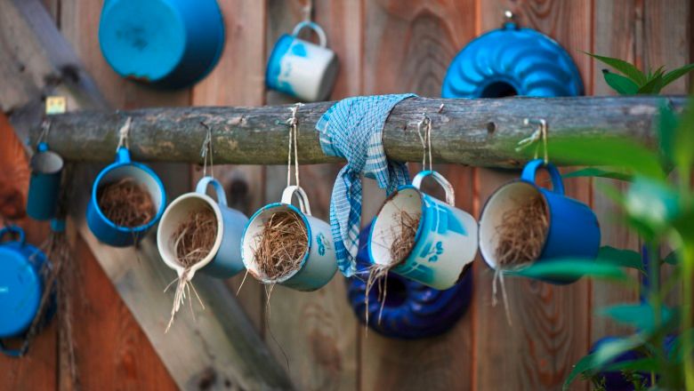 Blue enamel cups with straw hang from a wooden beam in front of a wooden wall.