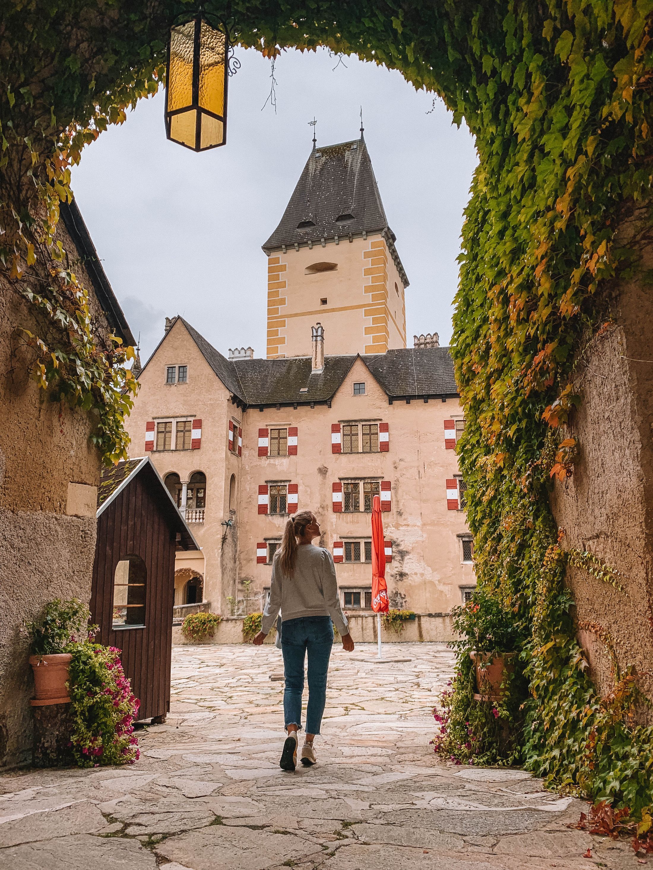 A person walks through an ivy-covered archway towards the inner courtyard of Ottenstein Castle.