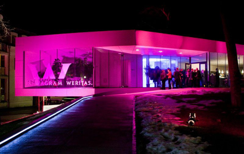 Modern wine bar at night with pink lighting and people at the entrance.