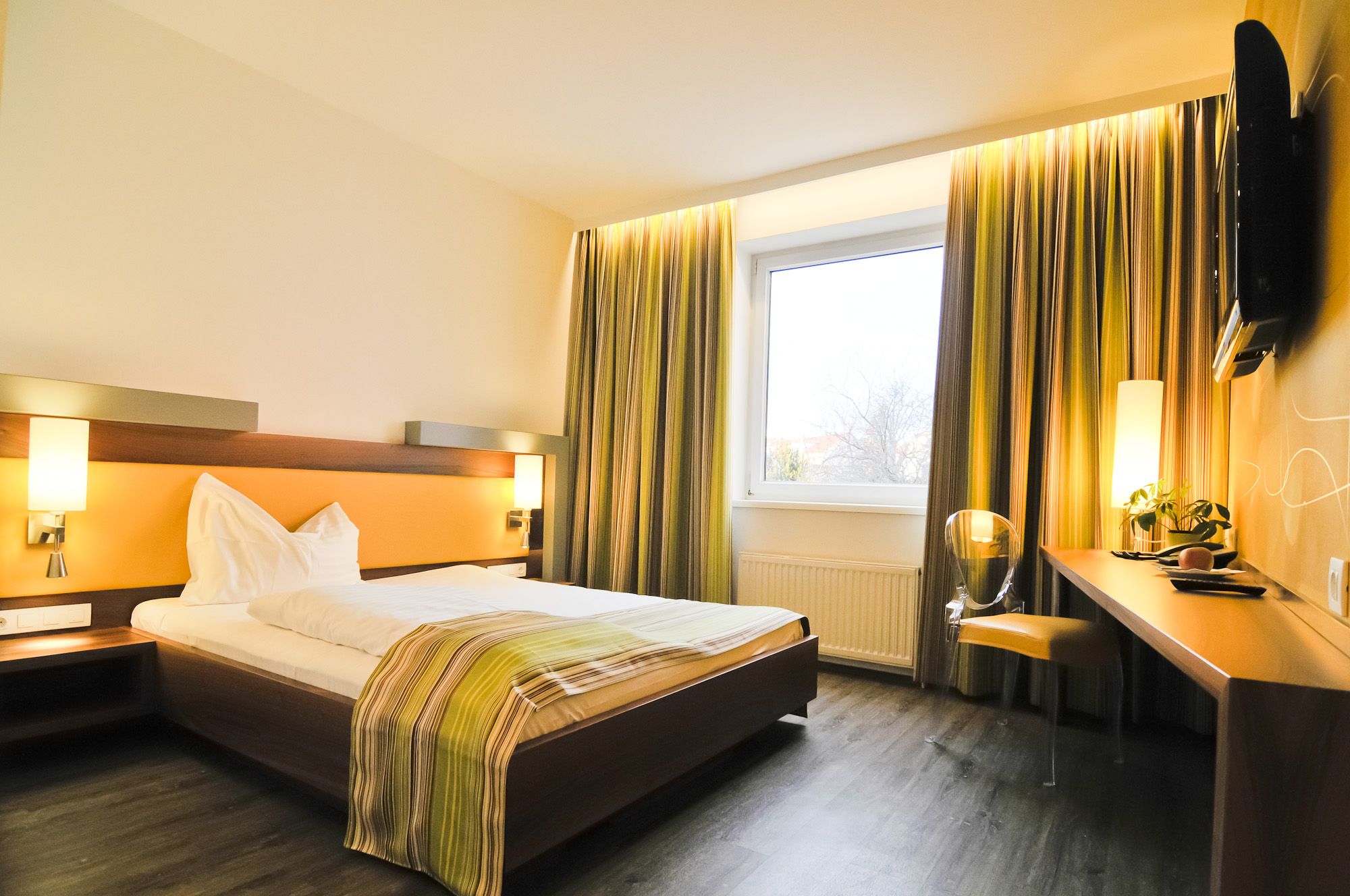 Modern hotel room with double bed, desk and large window.