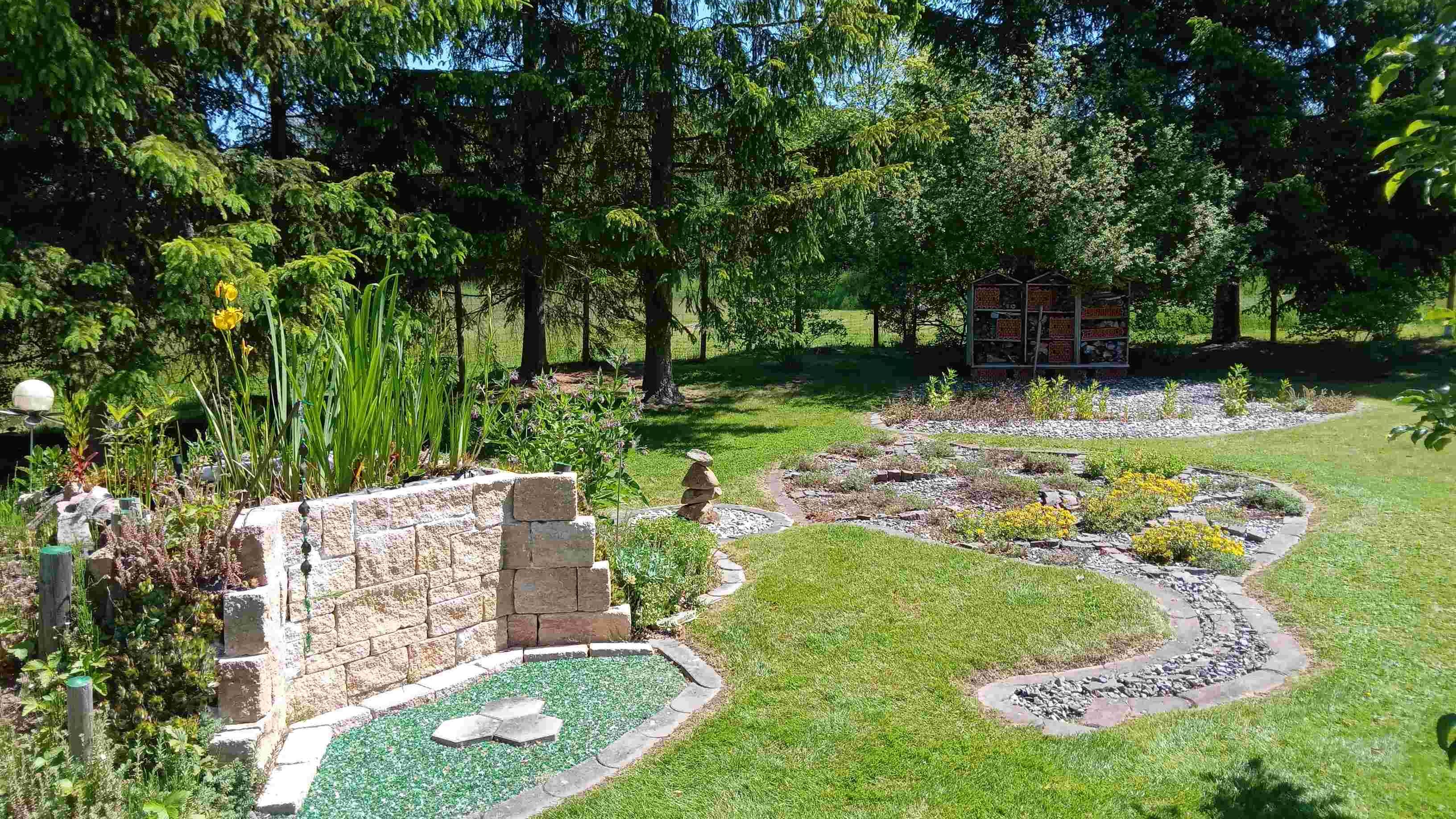 A well-tended garden with stones, plants and an insect hotel in the background.