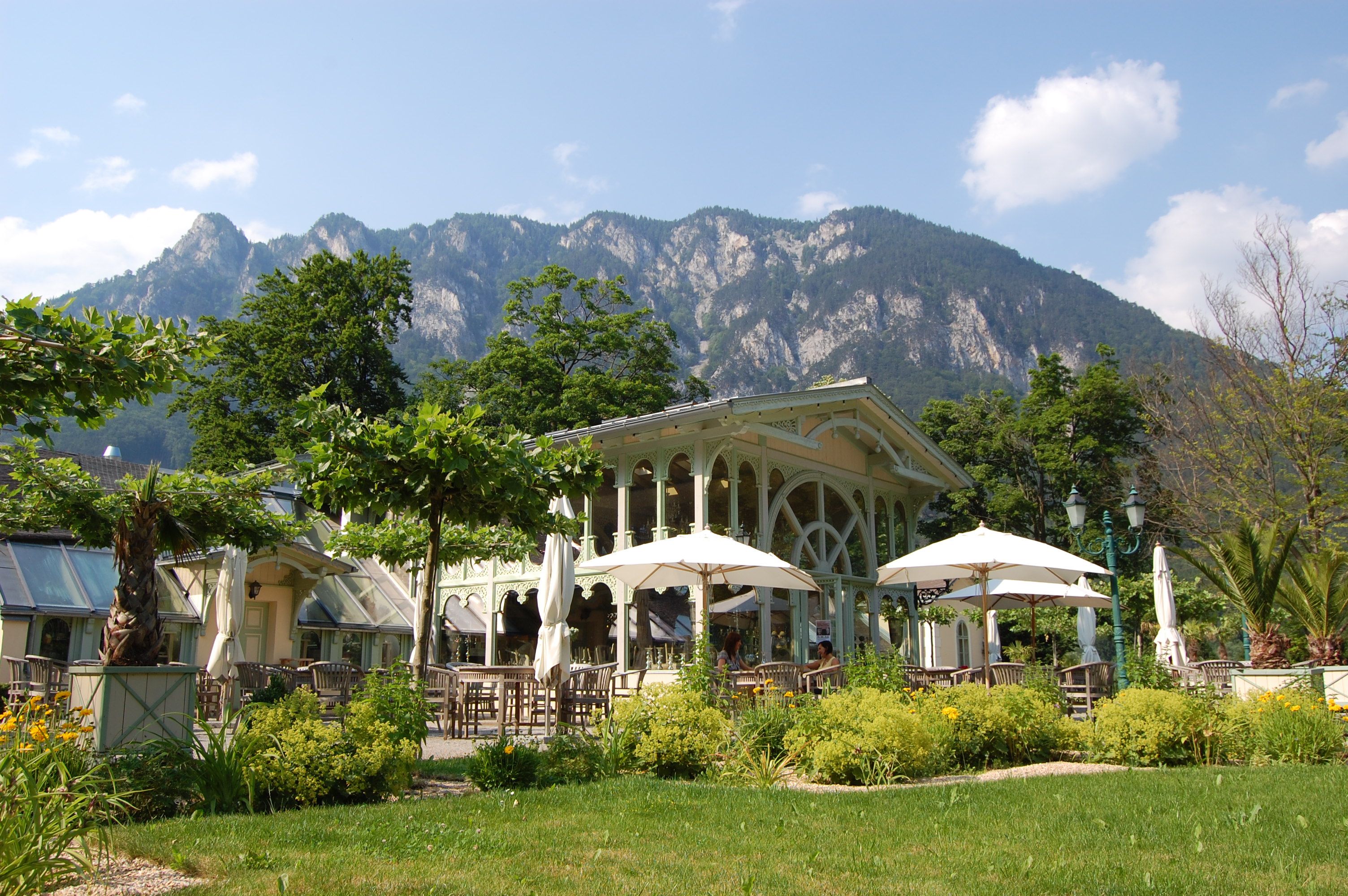 A garden pavilion with parasols and tables against a mountain backdrop.