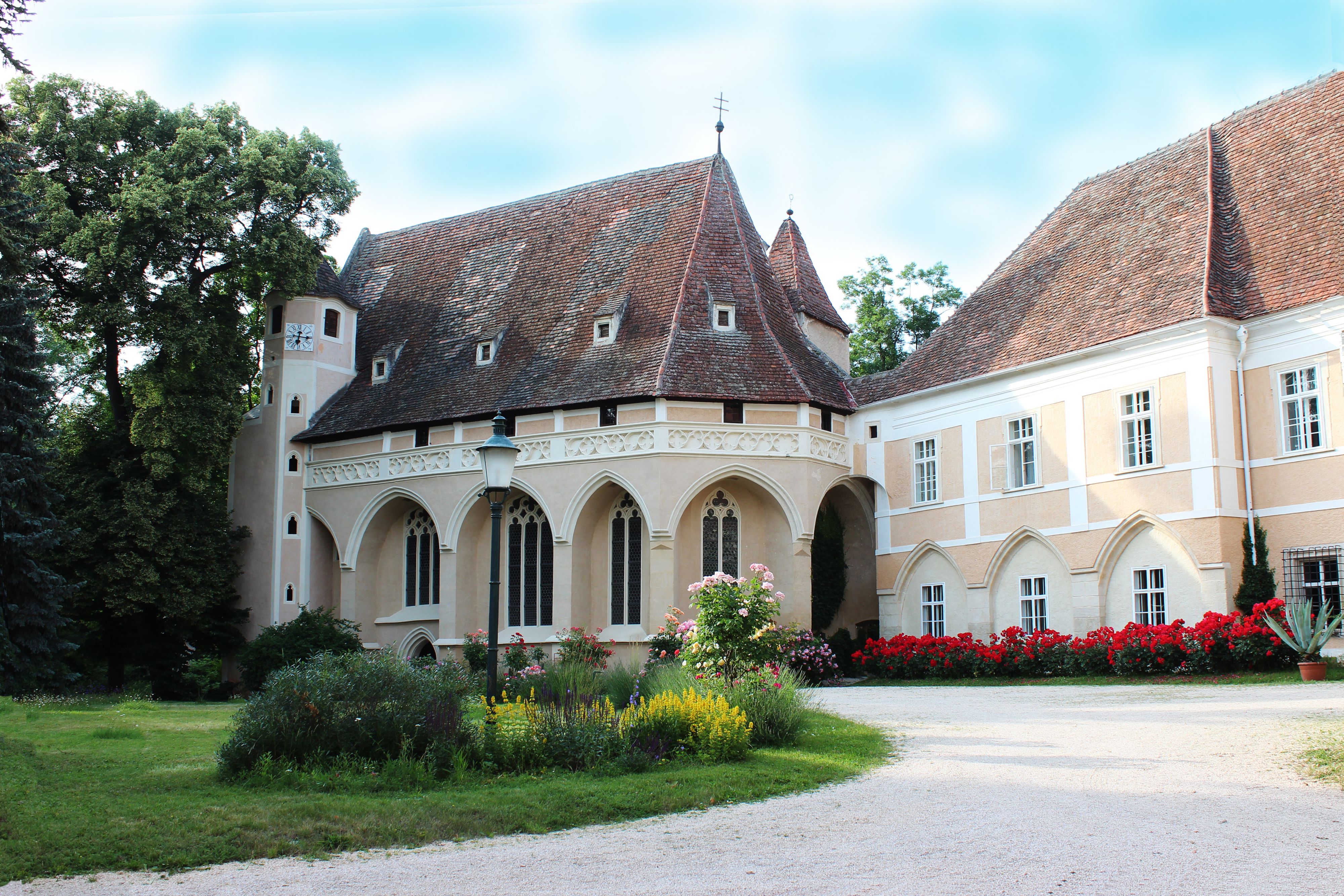 Historic building with pointed roof and garden in the foreground.