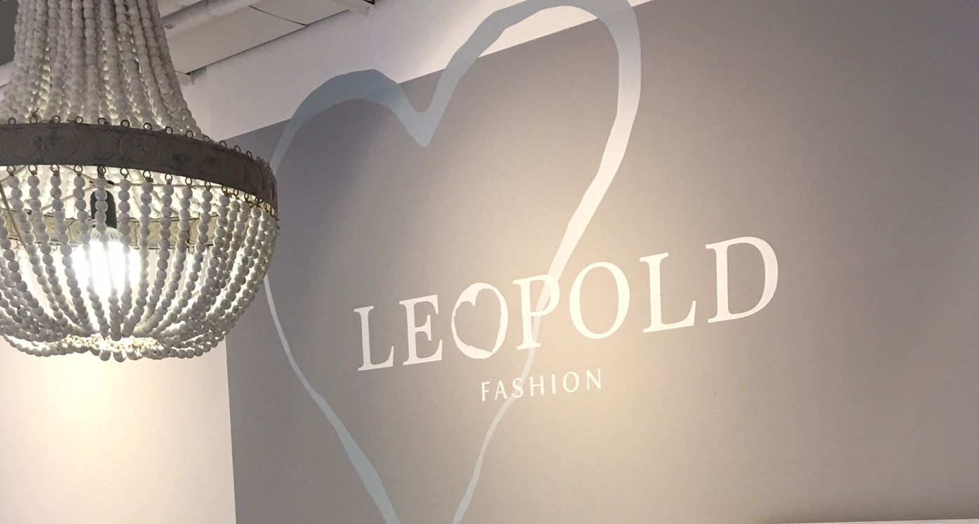 A chandelier hangs in front of a gray wall with the inscription 'LEOPOLD FASHION' and a heart motif.