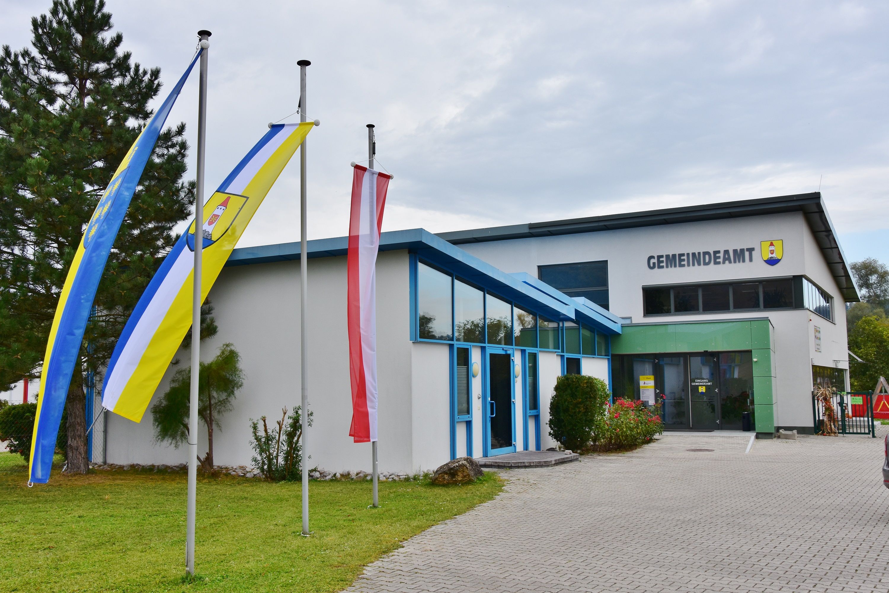 A modern building with the inscription 'Gemeindeamt' and three flagpoles in front of it.