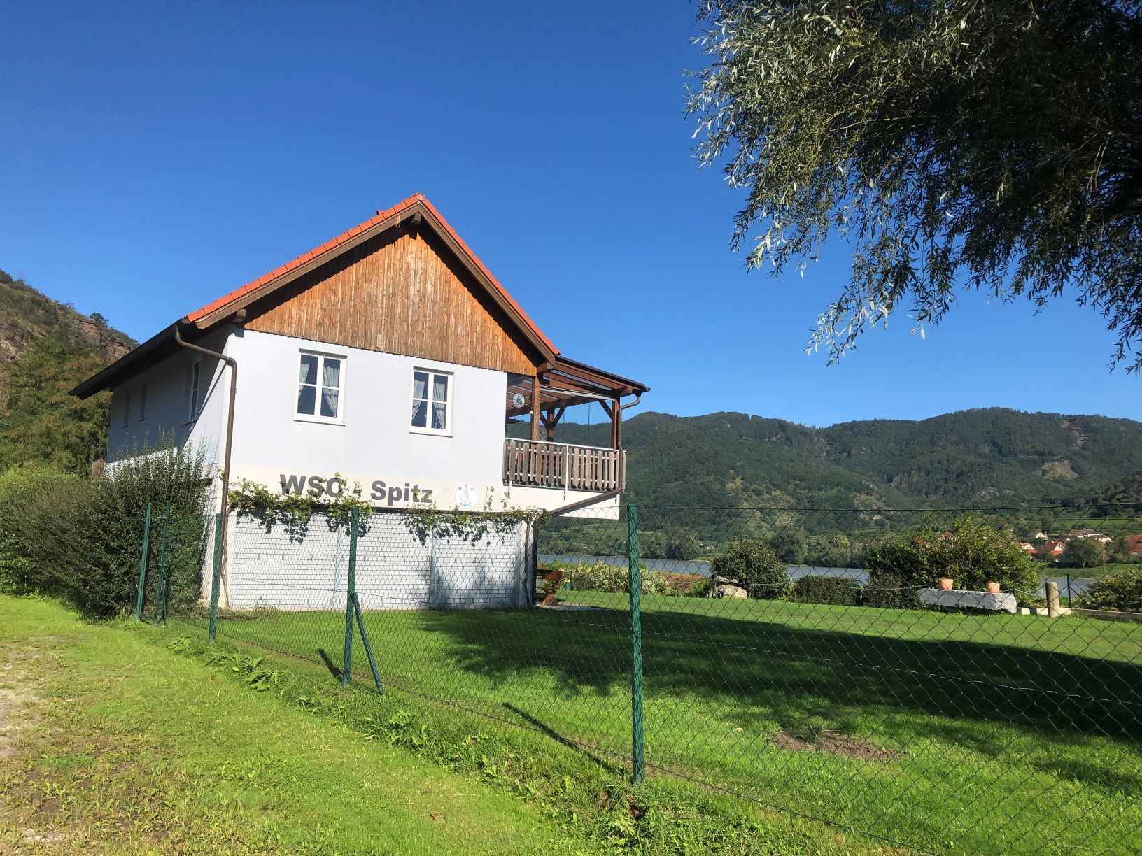 A clubhouse with the inscription 'WSC Spitz' in front of a mountain landscape.