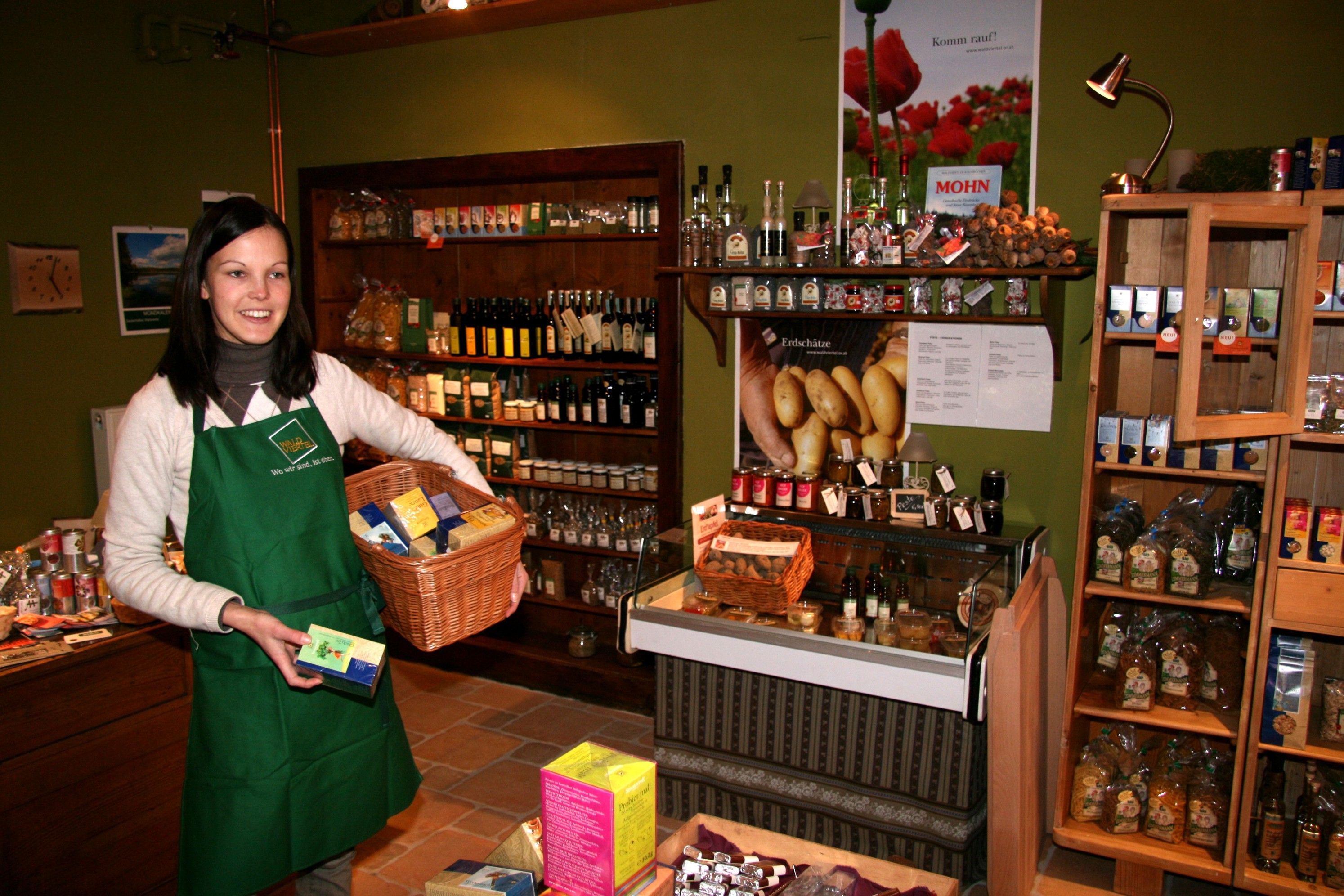 A woman in a store with a green apron holds a basket of products.