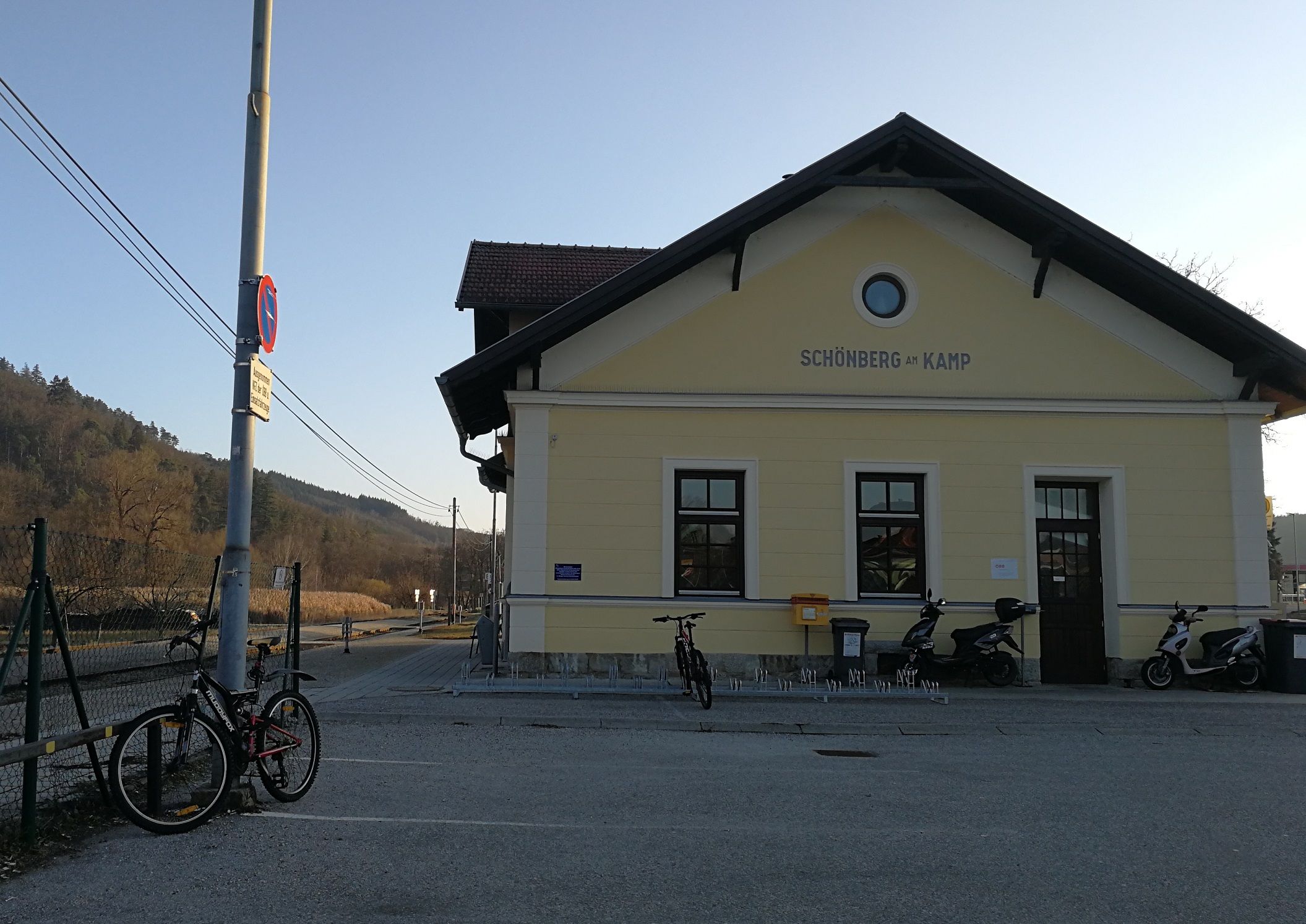 Schönberg am Kamp station with bicycles and scooters in front of it, surrounded by rural countryside.