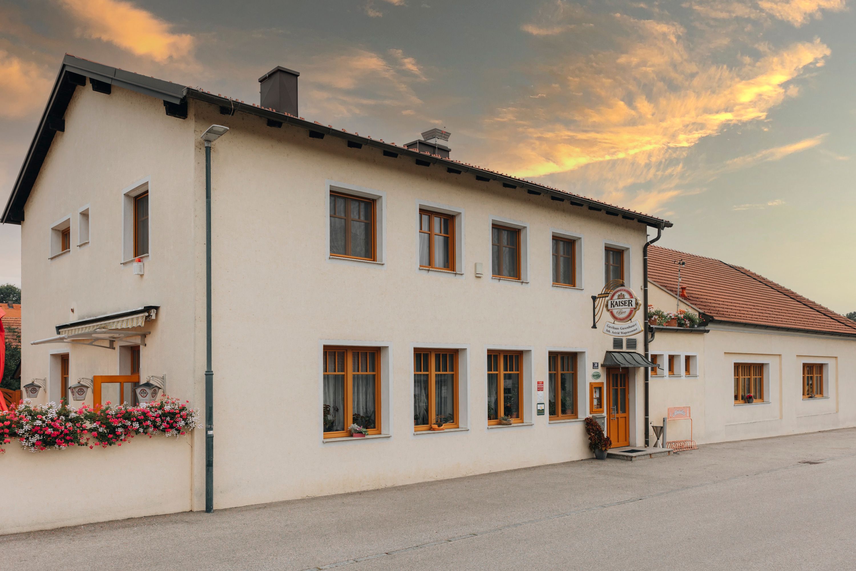 Inn with floral decorations and emperor's beer sign at sunset.