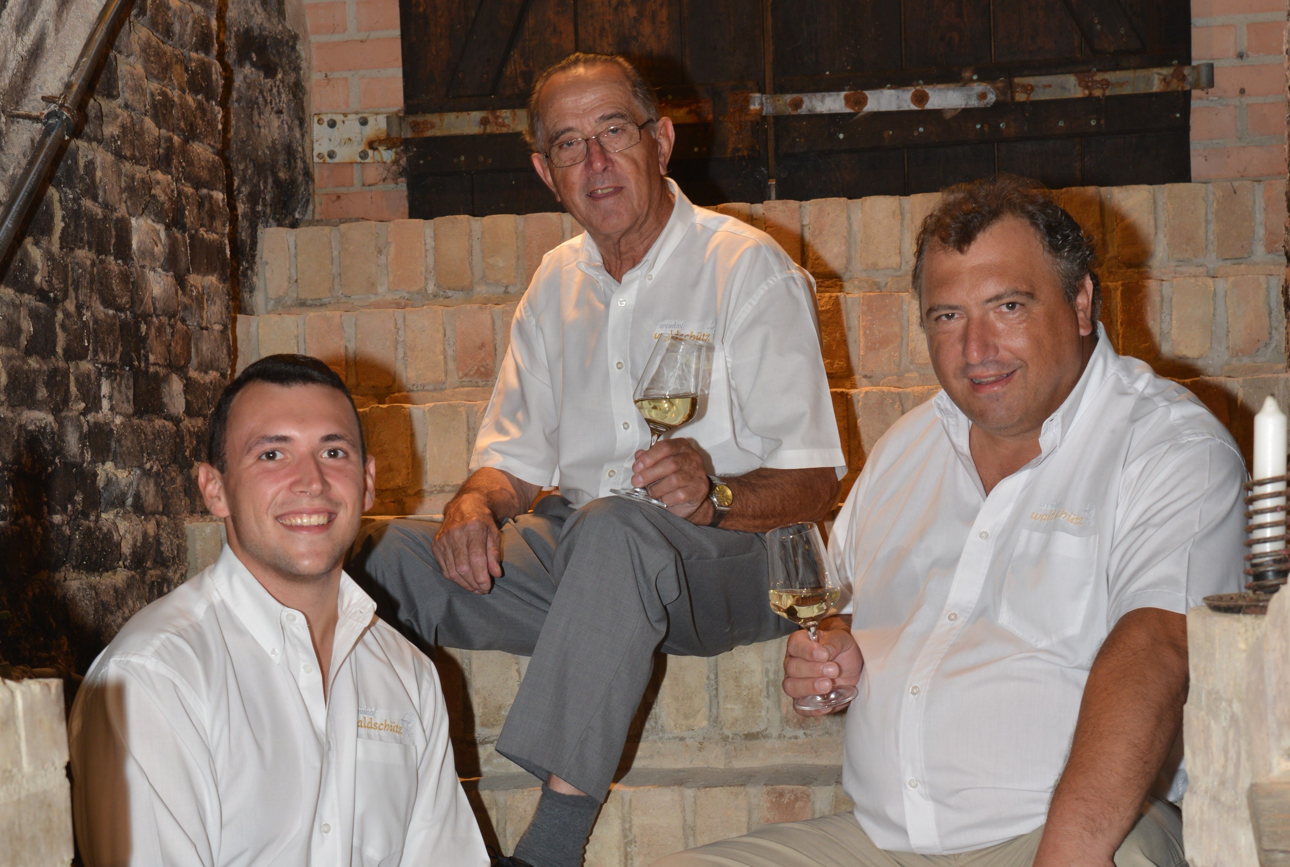 Three men in white shirts sit on a stone staircase holding wine glasses.