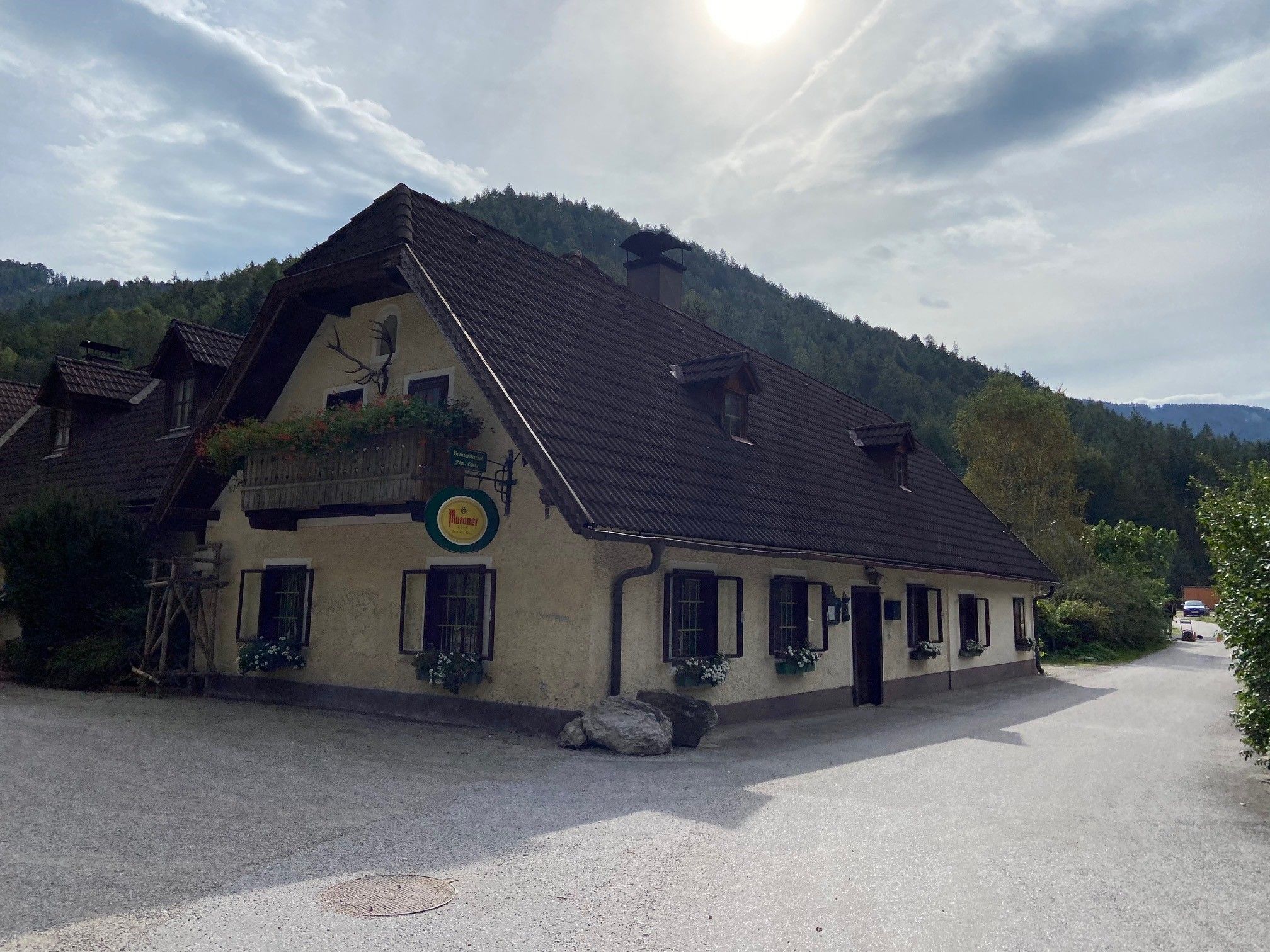 Traditional inn with flowered balcony in front of wooded hills.