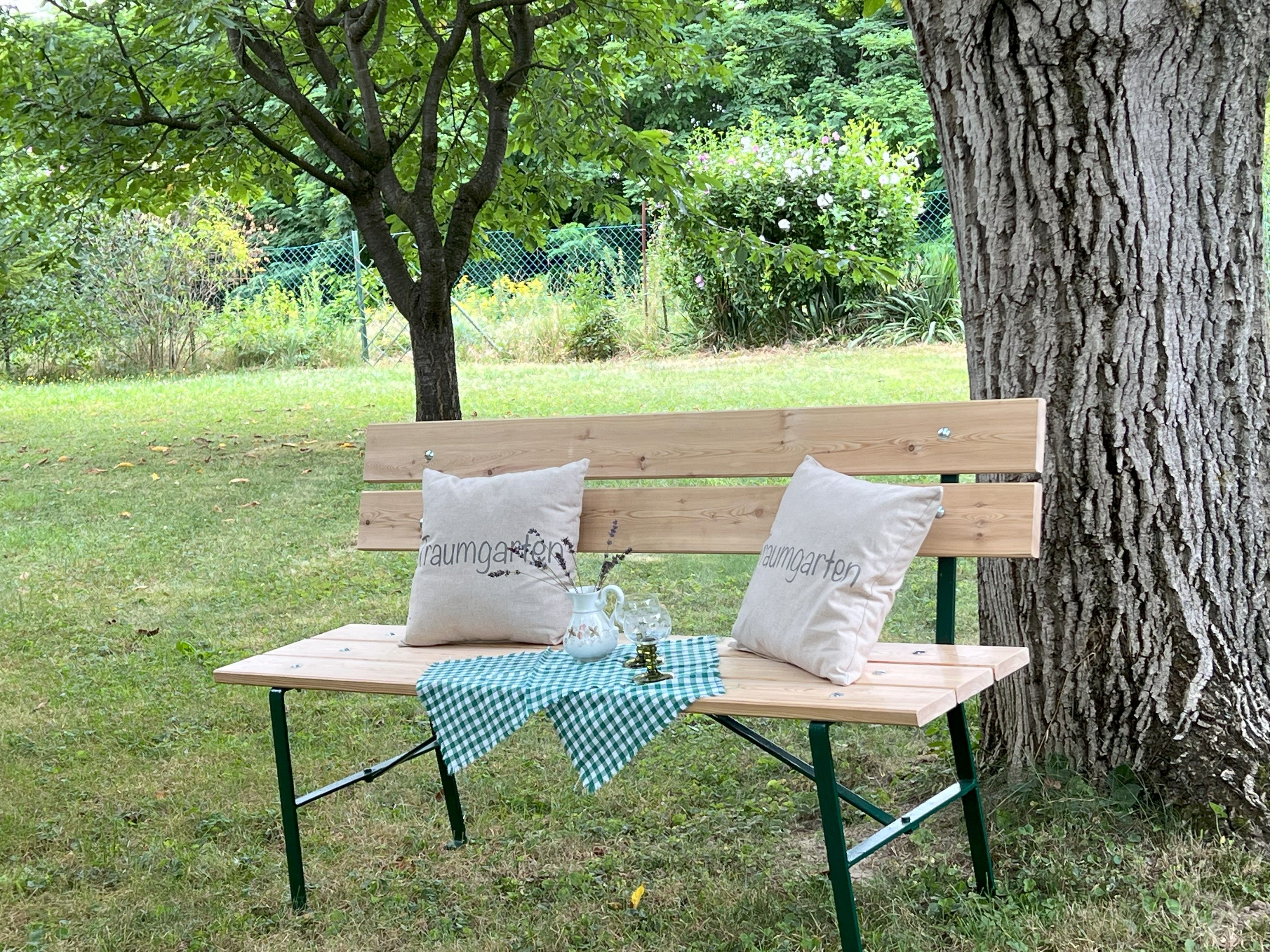 Wooden bench with cushions and tablecloth under a tree in the garden.