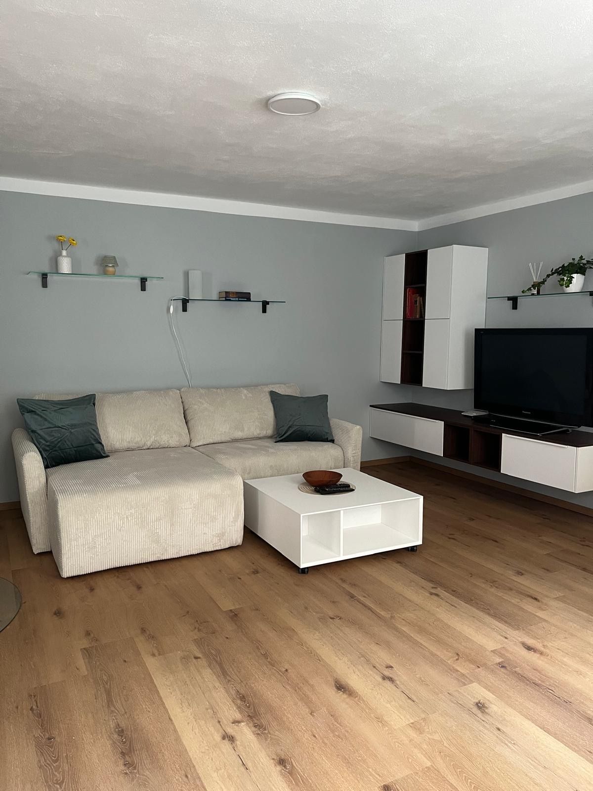 Modern living room with beige couch, white coffee table, wooden floor and wall shelves.