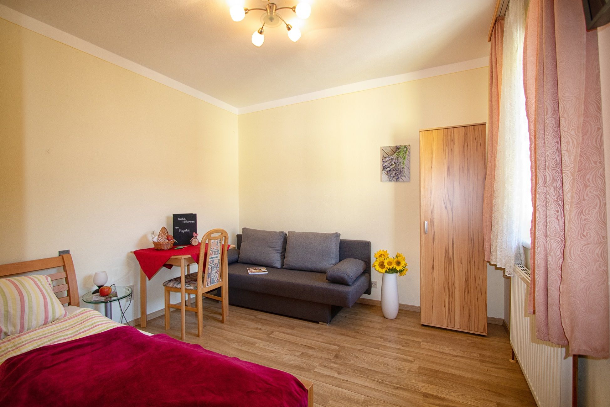 Cozy room with bed, sofa, table and wardrobe, decorated with sunflowers and a picture on the wall.