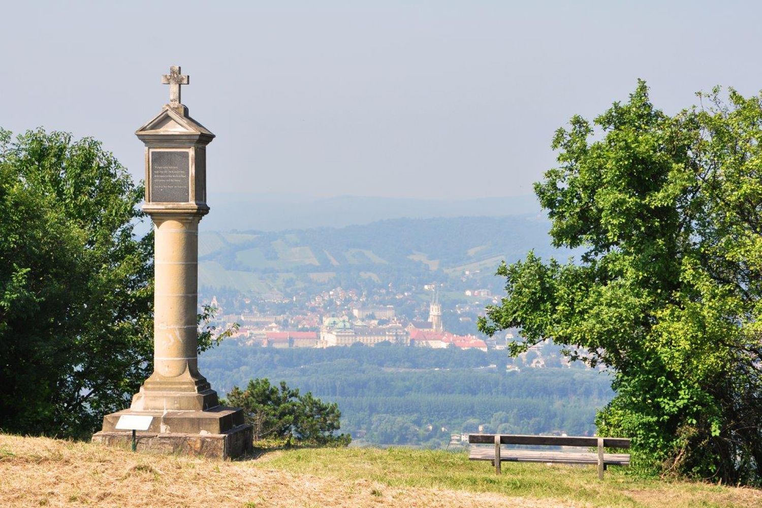 Column with cross on a hill, in the background a town and hills.