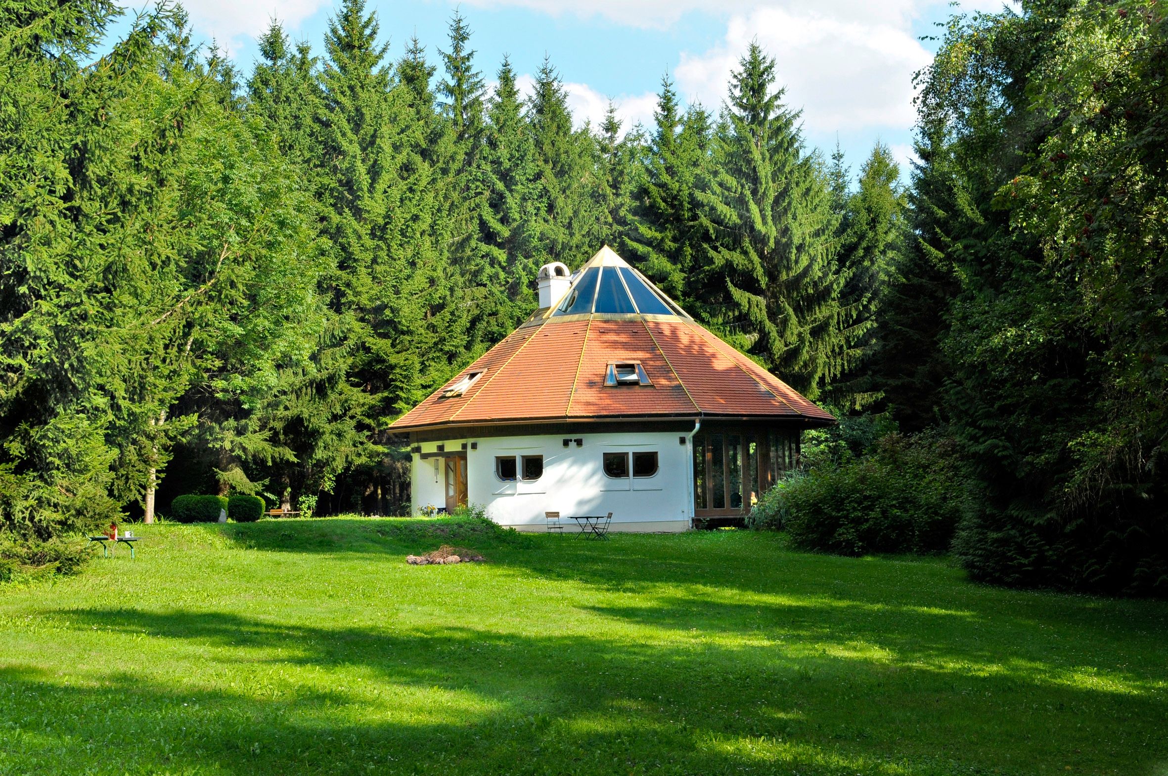 A round house with a pyramid roof in the middle of a forest.
