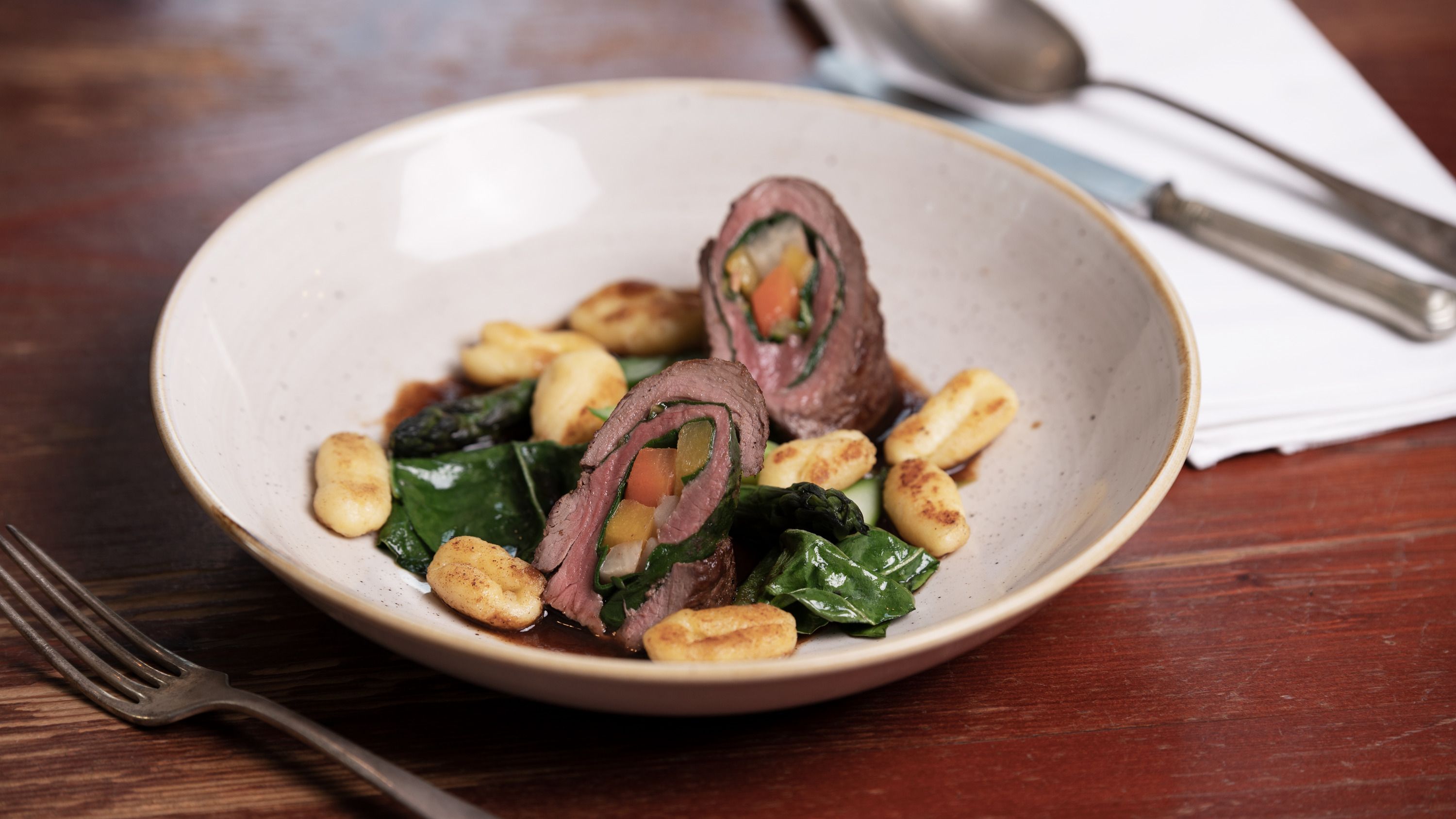Venison roulade with chard and root vegetables, served with gnocchi on a plate.