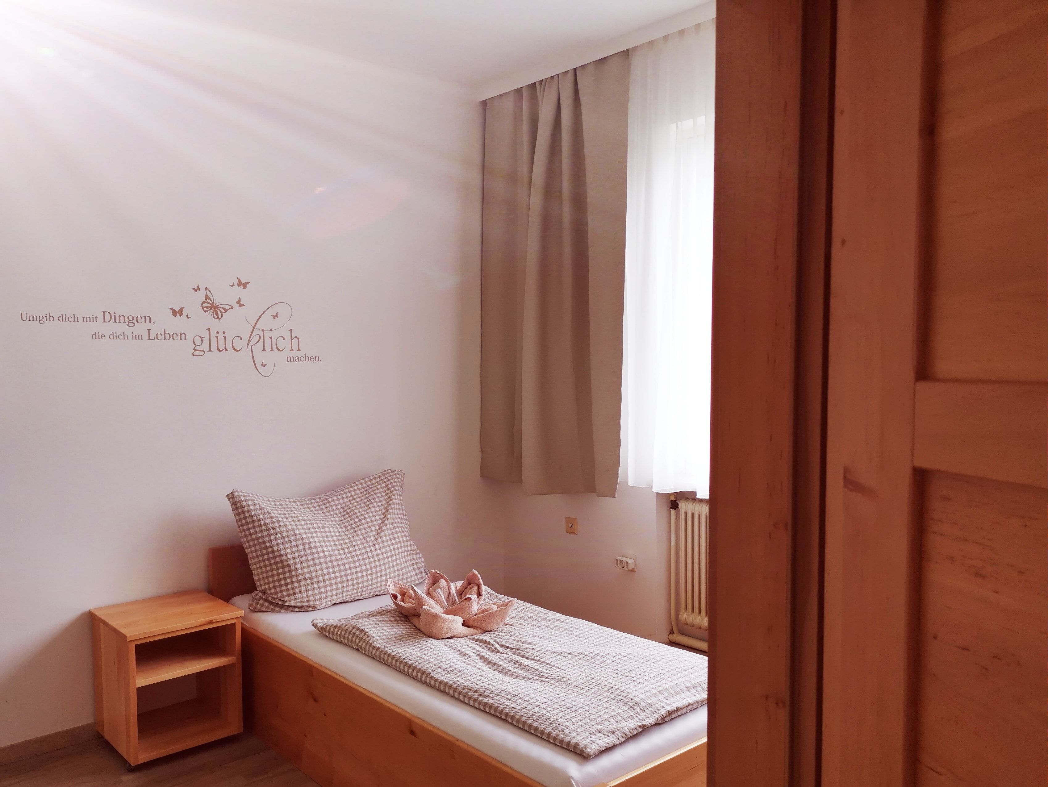 A simple guest room with a single bed, wooden shelf and a quote on the wall.