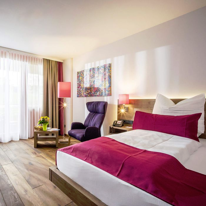Cozy room with double bed, wing chair, table, lamps, a mural and wooden floor.