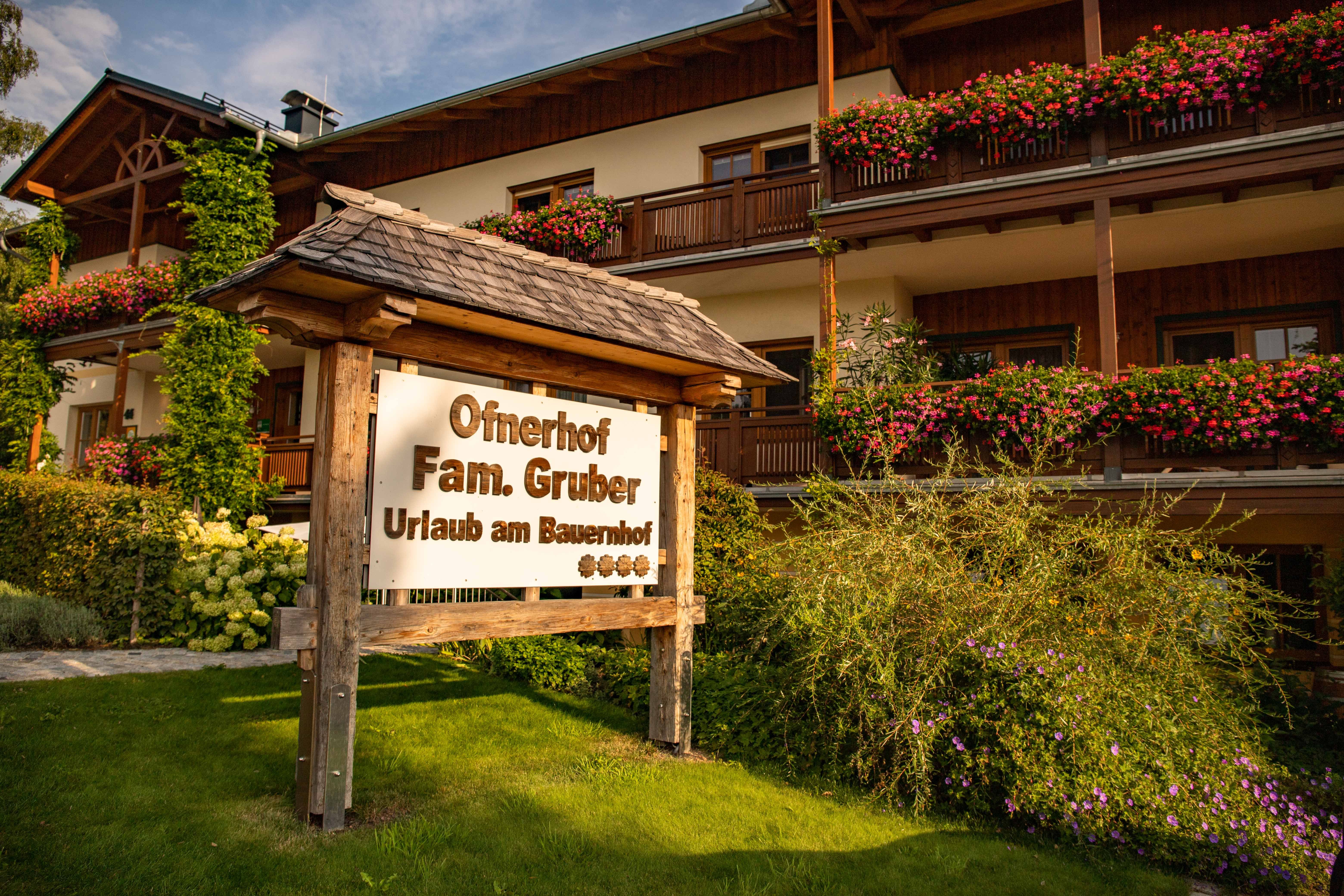 Sign in front of a farm with flowers and wooden veranda.