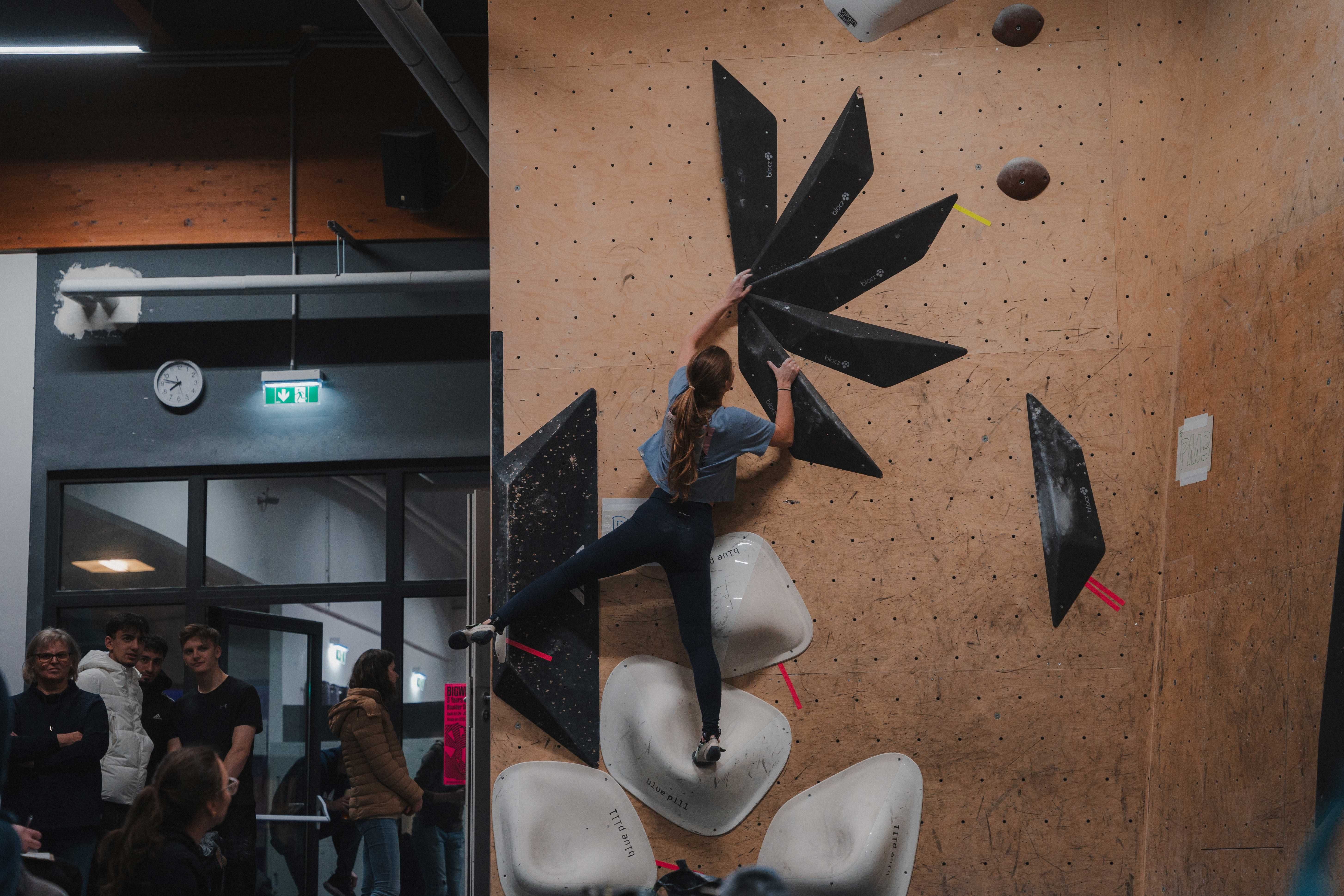 A woman climbs on an indoor climbing wall with black and white holds.