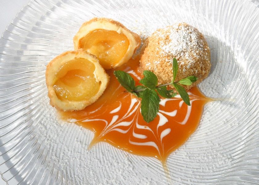 Wachau apricot dumplings on a plate decorated with apricot sauce and mint leaves.