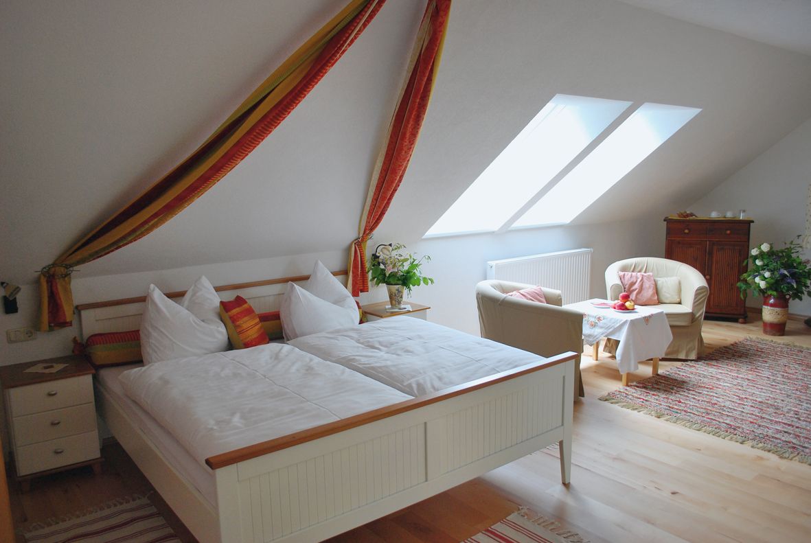 Cozy bedroom with double bed, armchairs and table under a sloping roof.