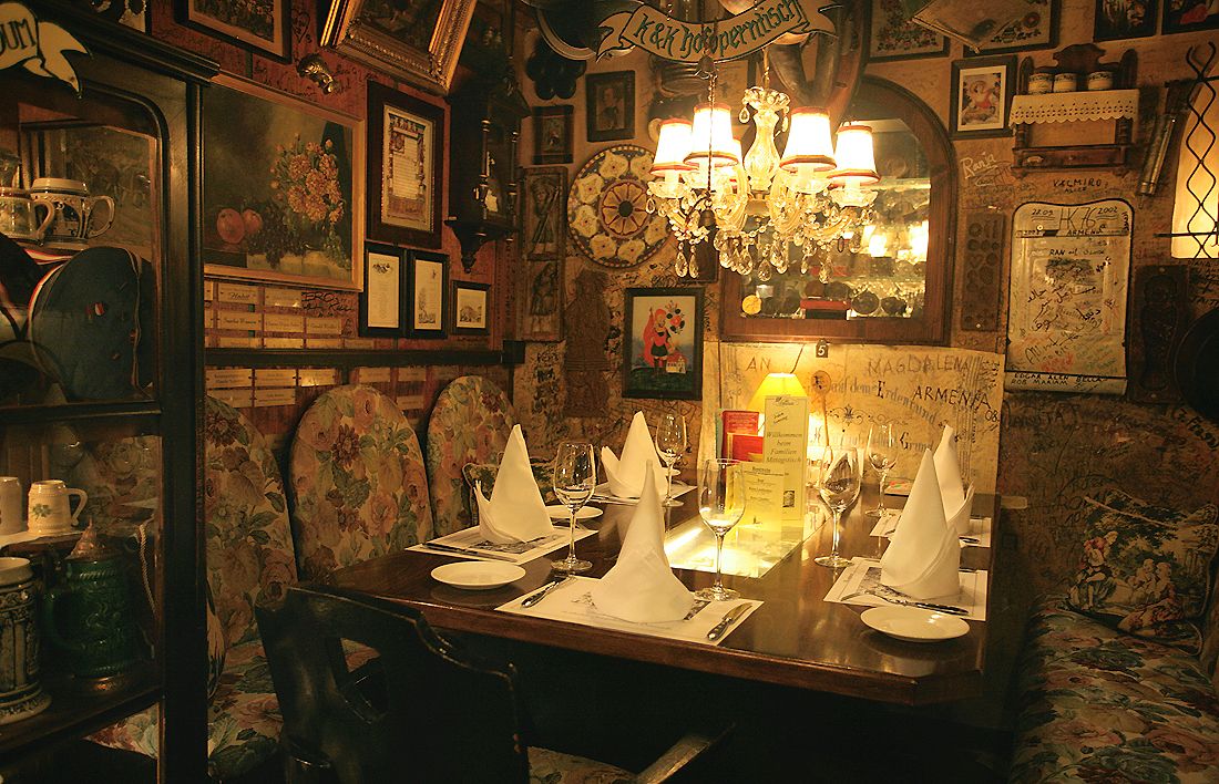 Comfortably decorated restaurant with a table setting, chandelier and pictures on the walls.