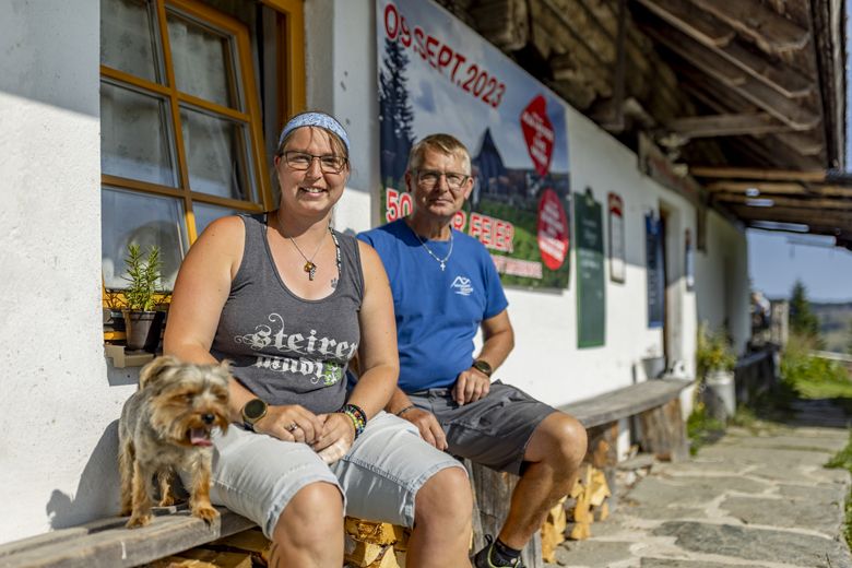 Two people sitting in front of a building with a dog, in the background a poster with the date Sept. 09, 2023.