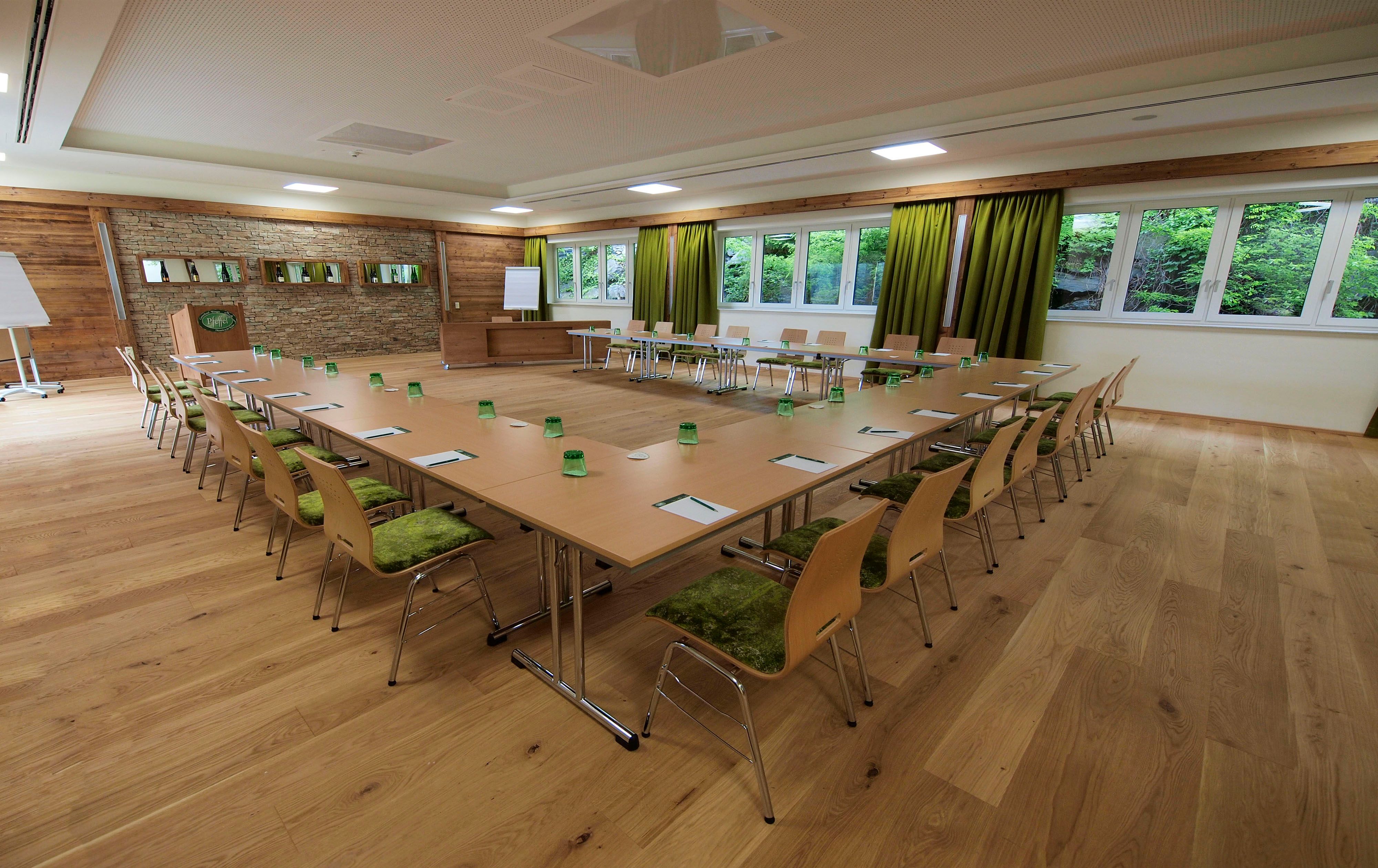 Seminar room with U-shaped table arrangement, green chairs and large windows.