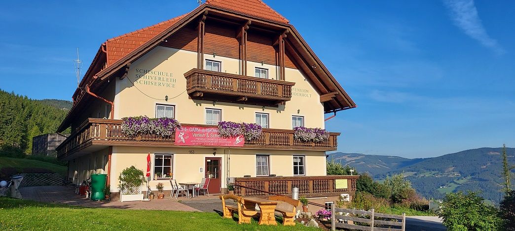 A traditional inn with wooden balconies and flowers, surrounded by green hills and blue skies.