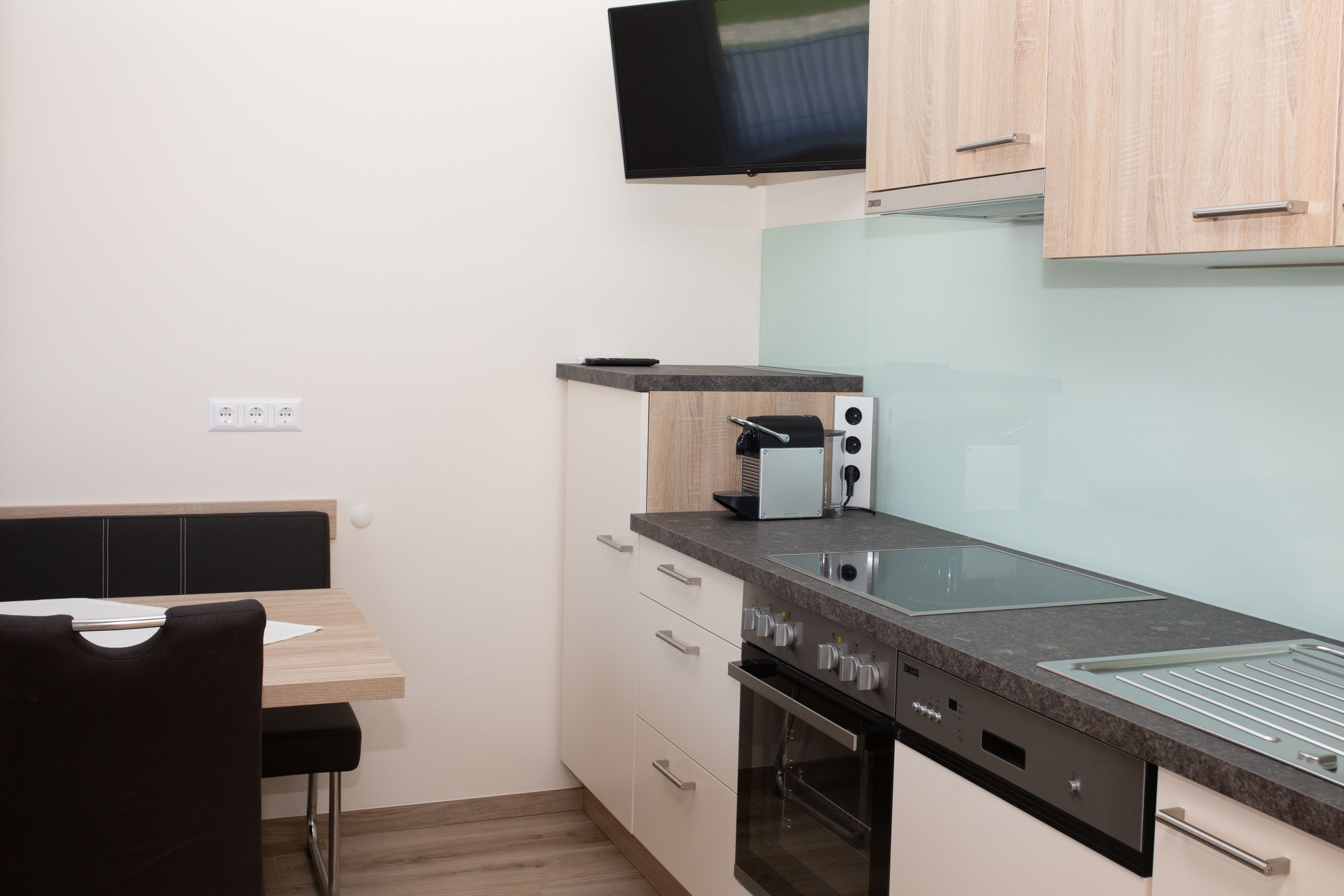 Modern kitchen with stove, sink, coffee machine and wall-mounted TV.
