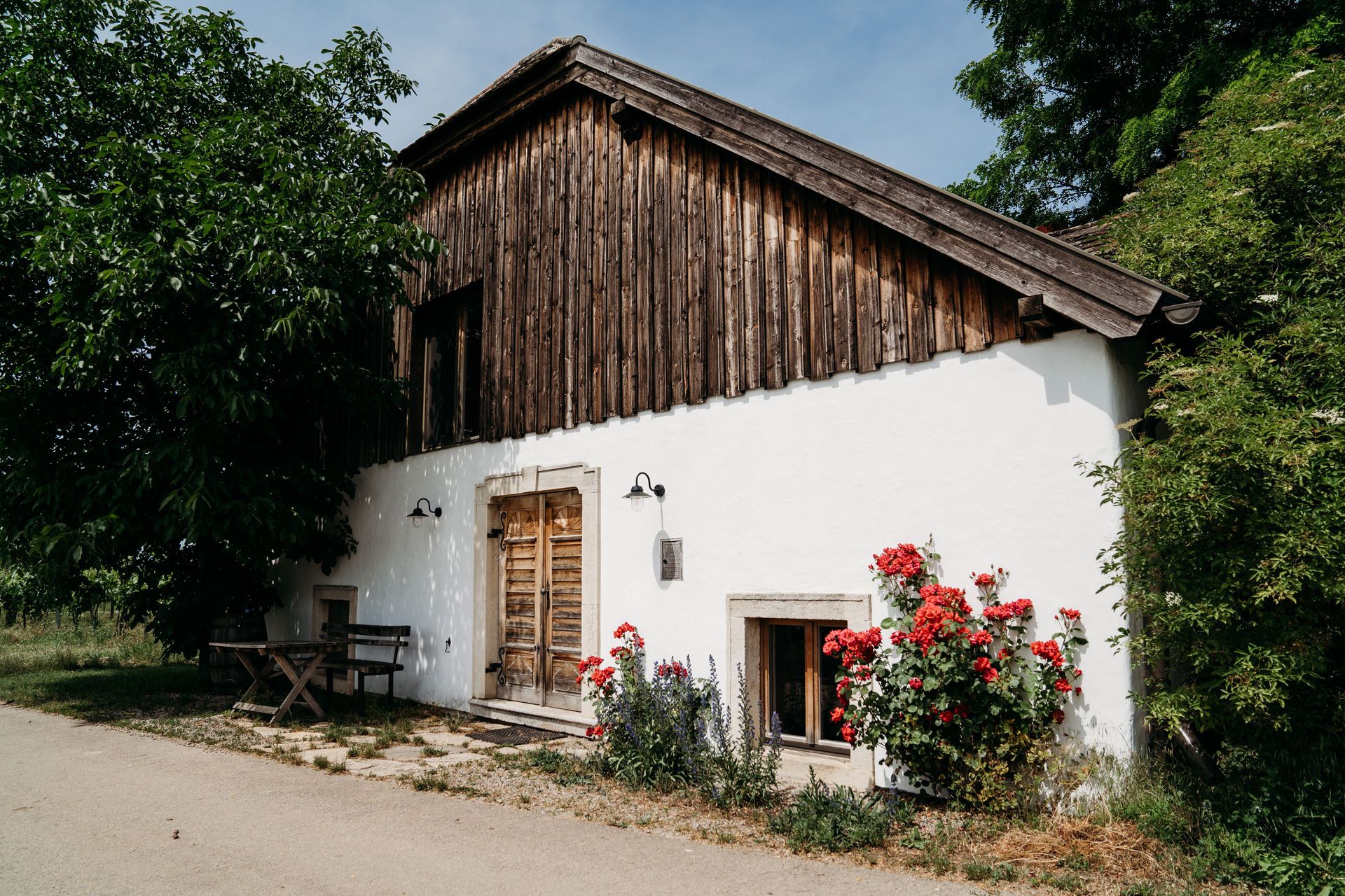 Exterior view of a house with wooden walls, white walls and red flowers in the foreground.