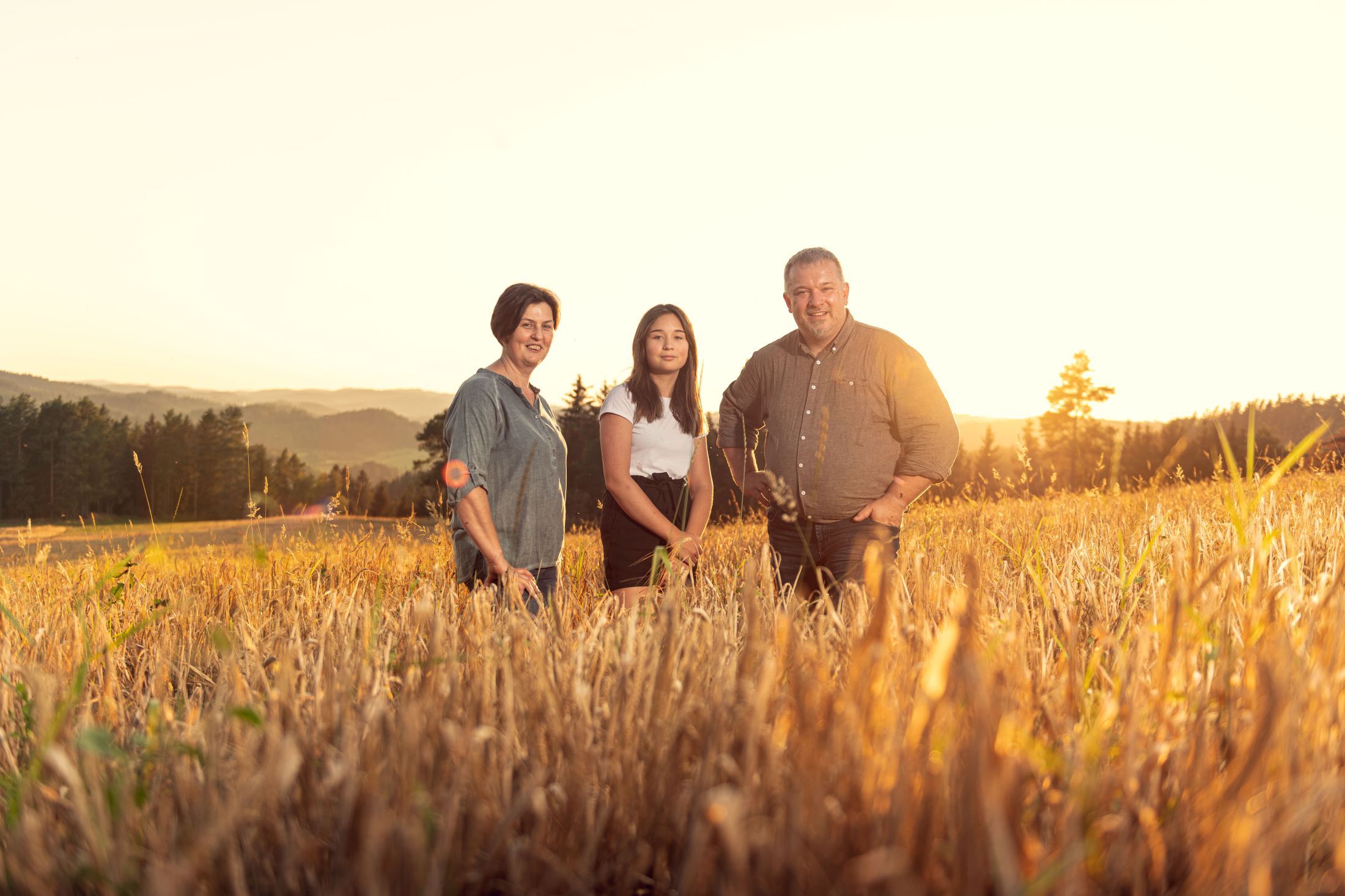 Three people stand in a field at sunset.