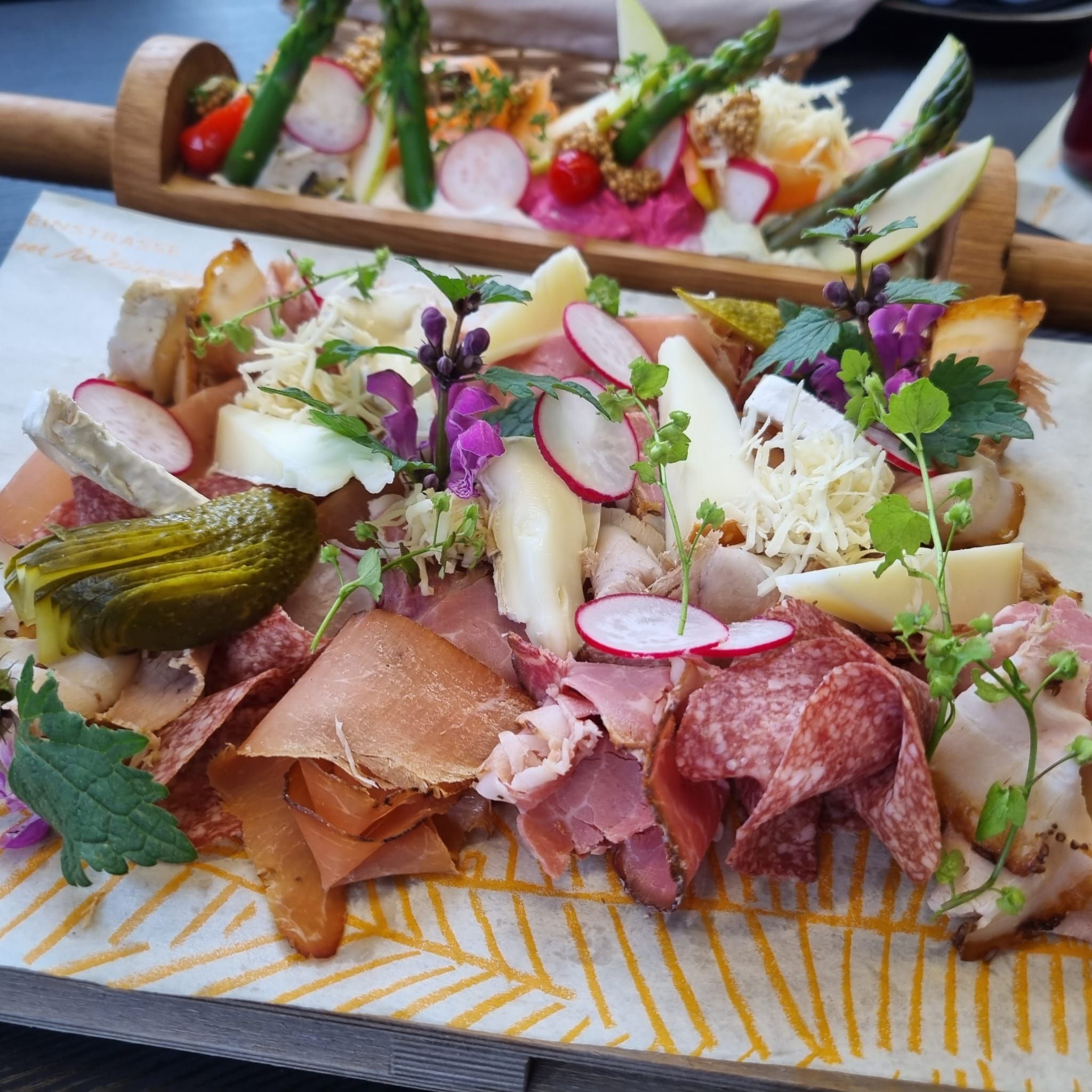 A Heurigen platter with various types of sausage and cheese, radishes, gherkins and herbs served on a wooden board.