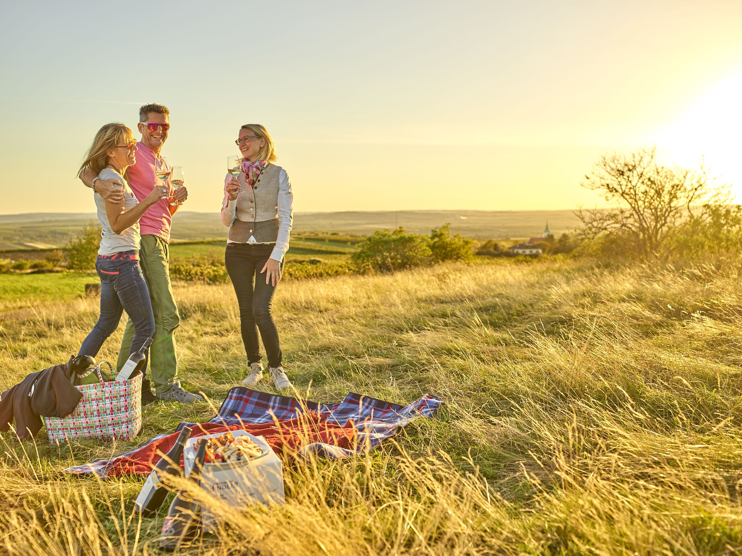 Three people having a picnic in a meadow at sunset.