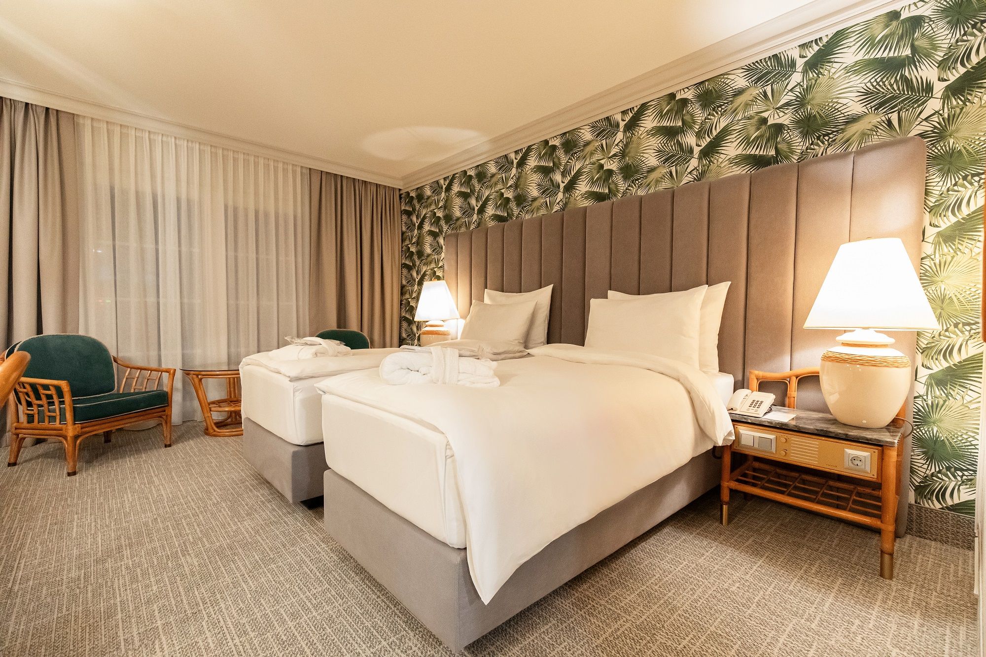 Hotel room with two single beds, tropical wallpaper and bedside lamps.