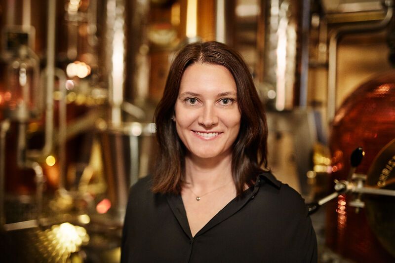 Woman in black blouse in front of distillation apparatus in a whisky distillery.