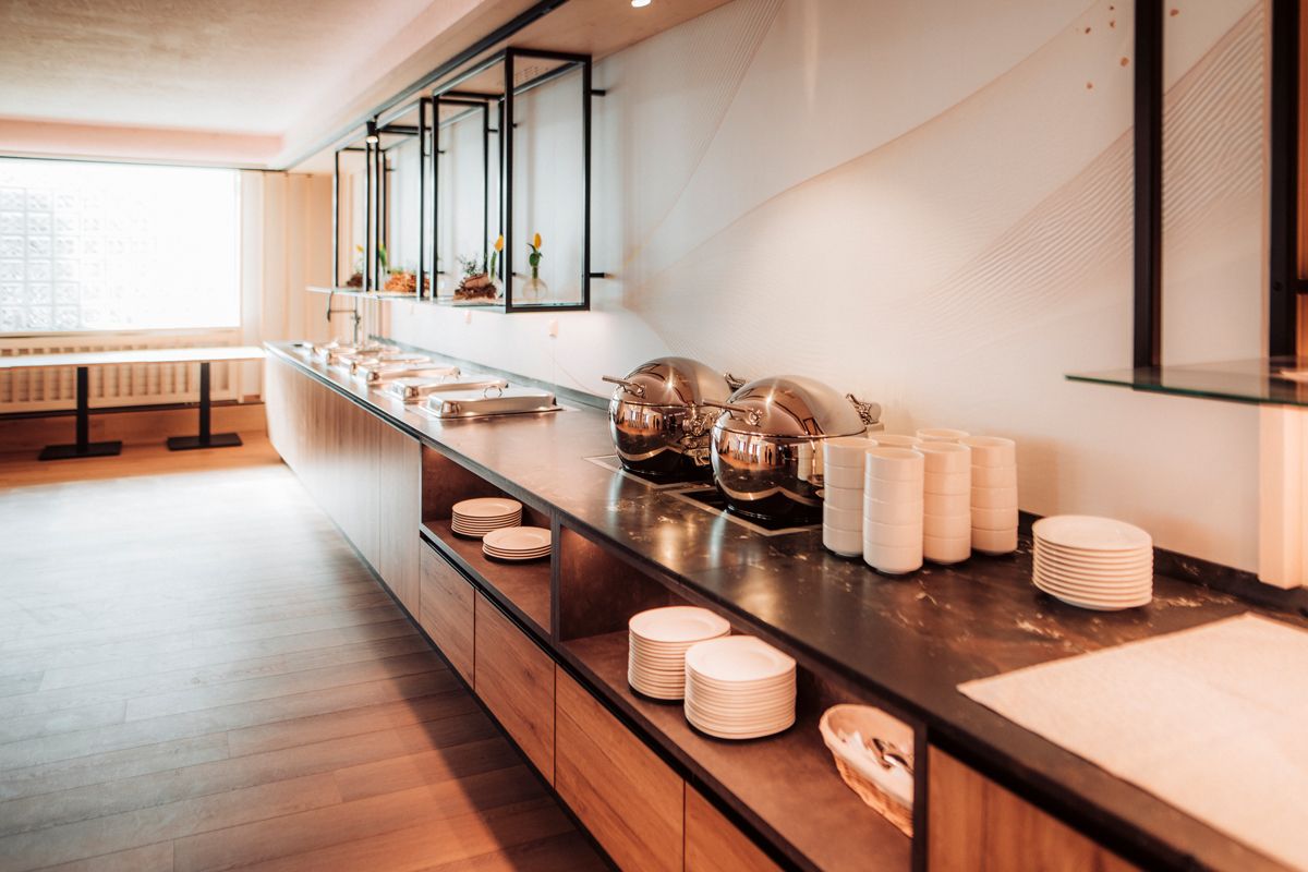 An elegant buffet with gleaming warming trays and stacked crockery in a modern room.