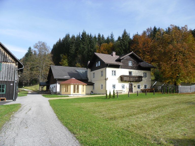 A large, two-story house with a balcony, surrounded by meadows and trees in autumn.