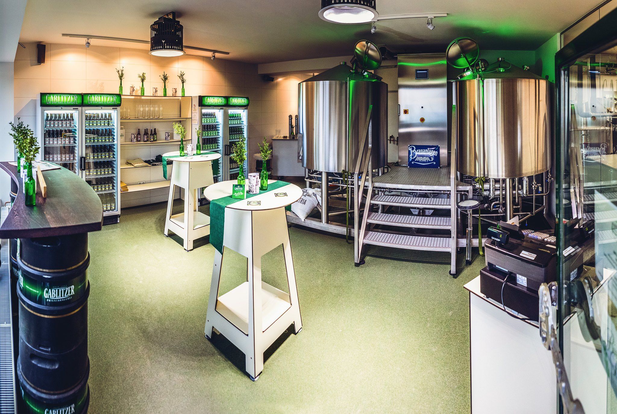 Interior view of a small brewery with stainless steel kettles and fridges full of drinks.