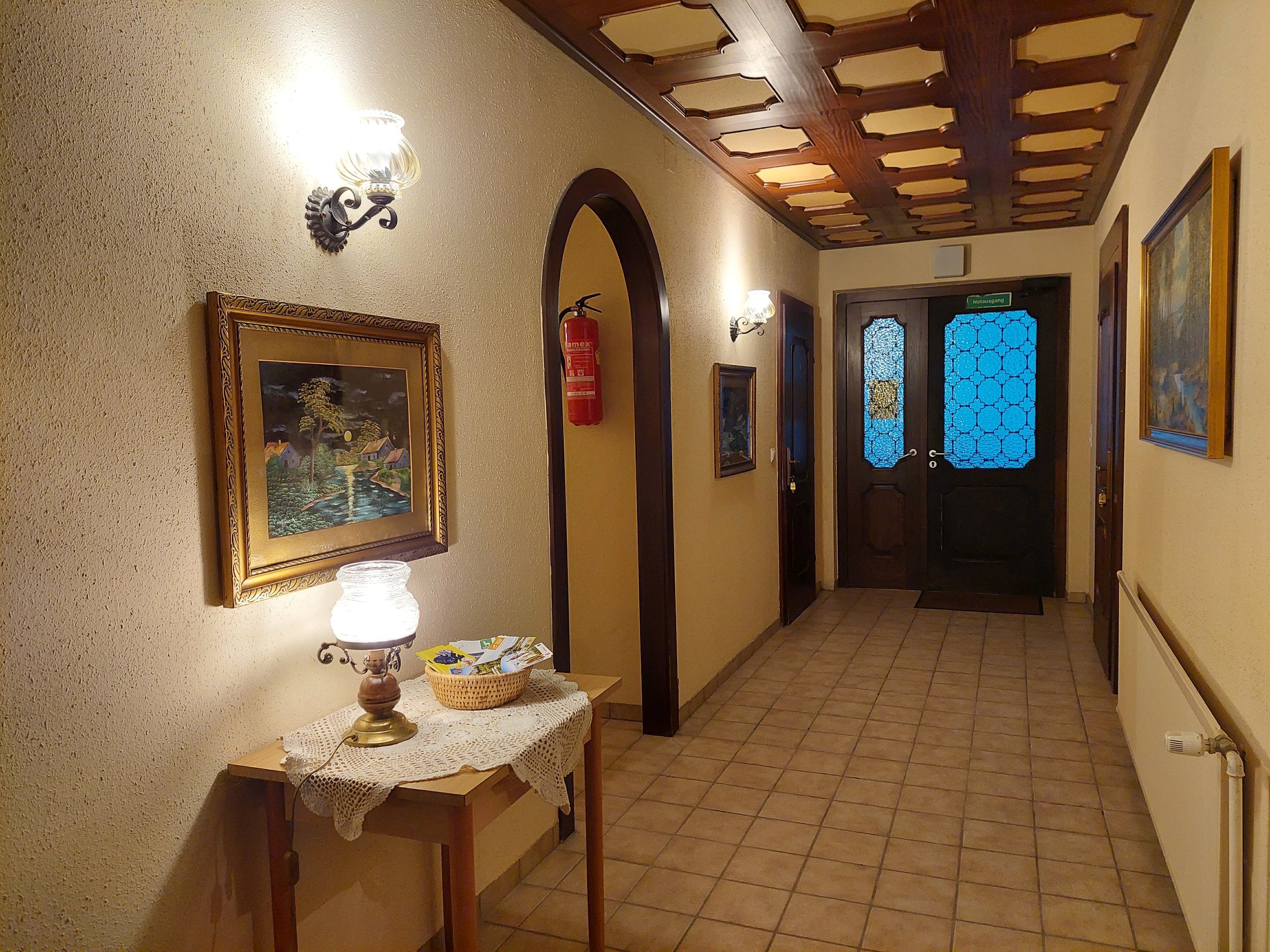 Interior view of a hallway with wooden table, lamp, paintings and blue glass doors.