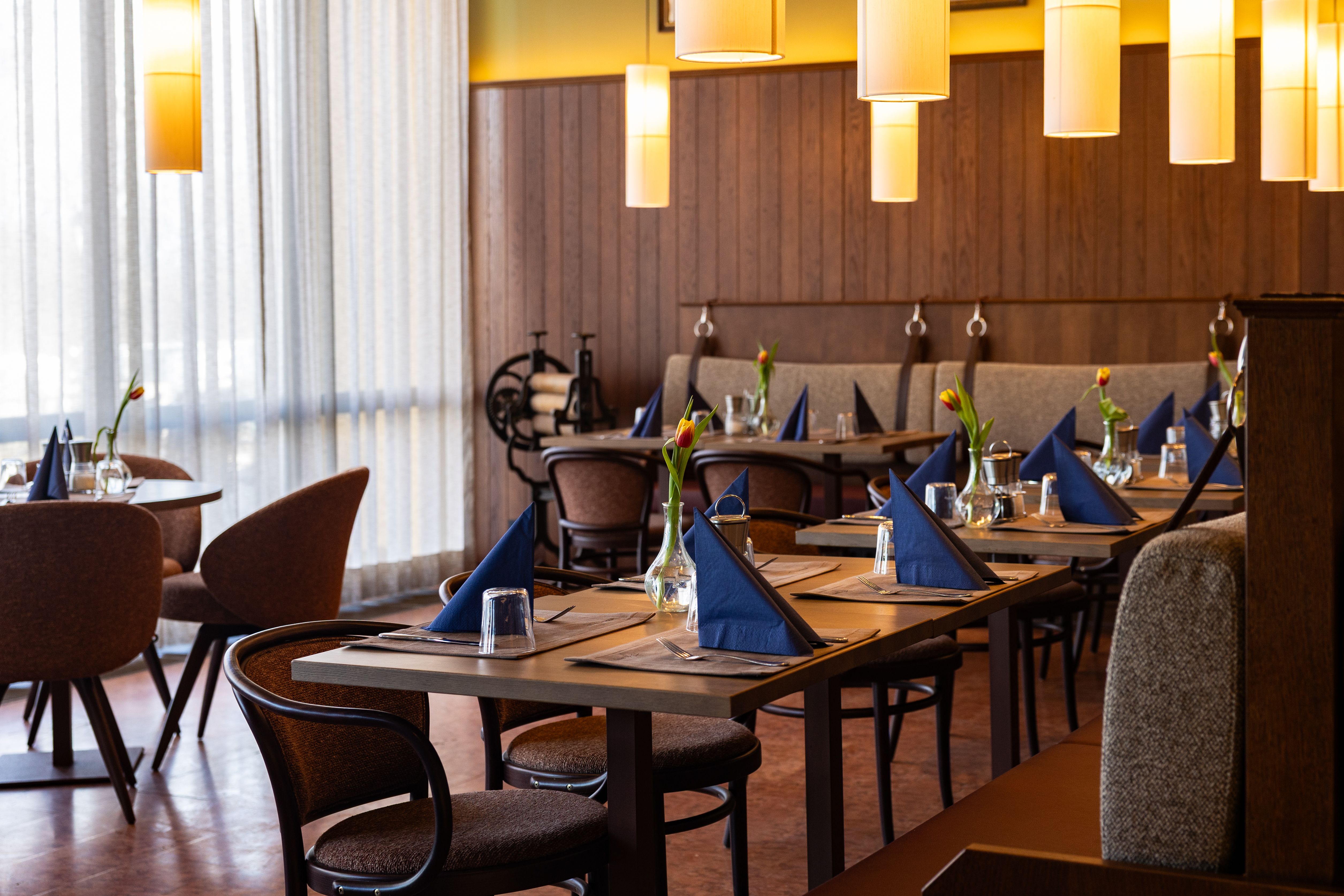 A stylishly furnished restaurant with laid tables, blue napkins and tulips in vases.