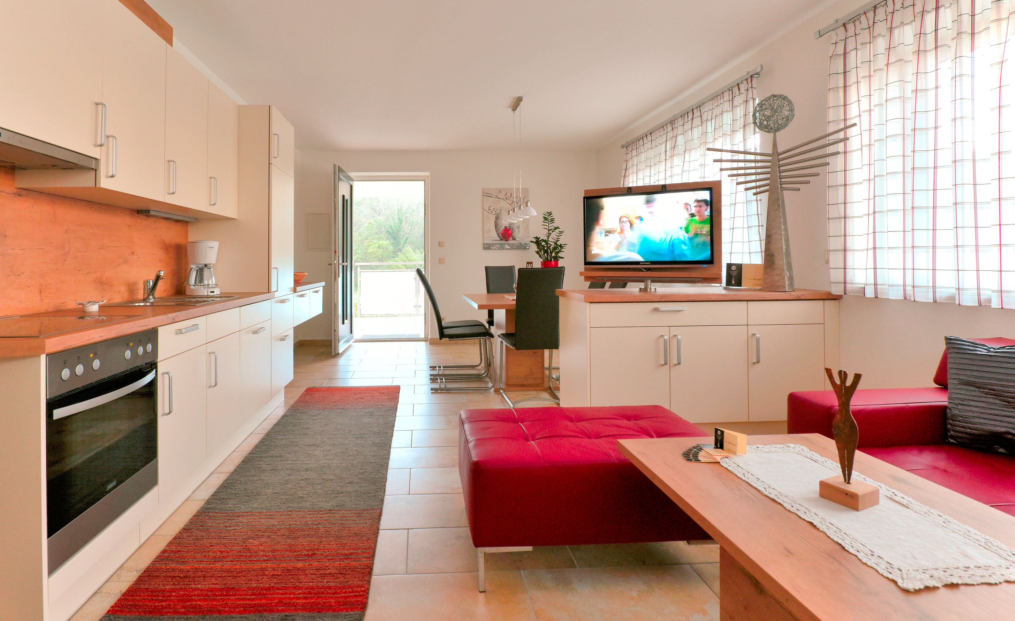 Modern eat-in kitchen with fitted kitchen, dining table, TV and red seating furniture.