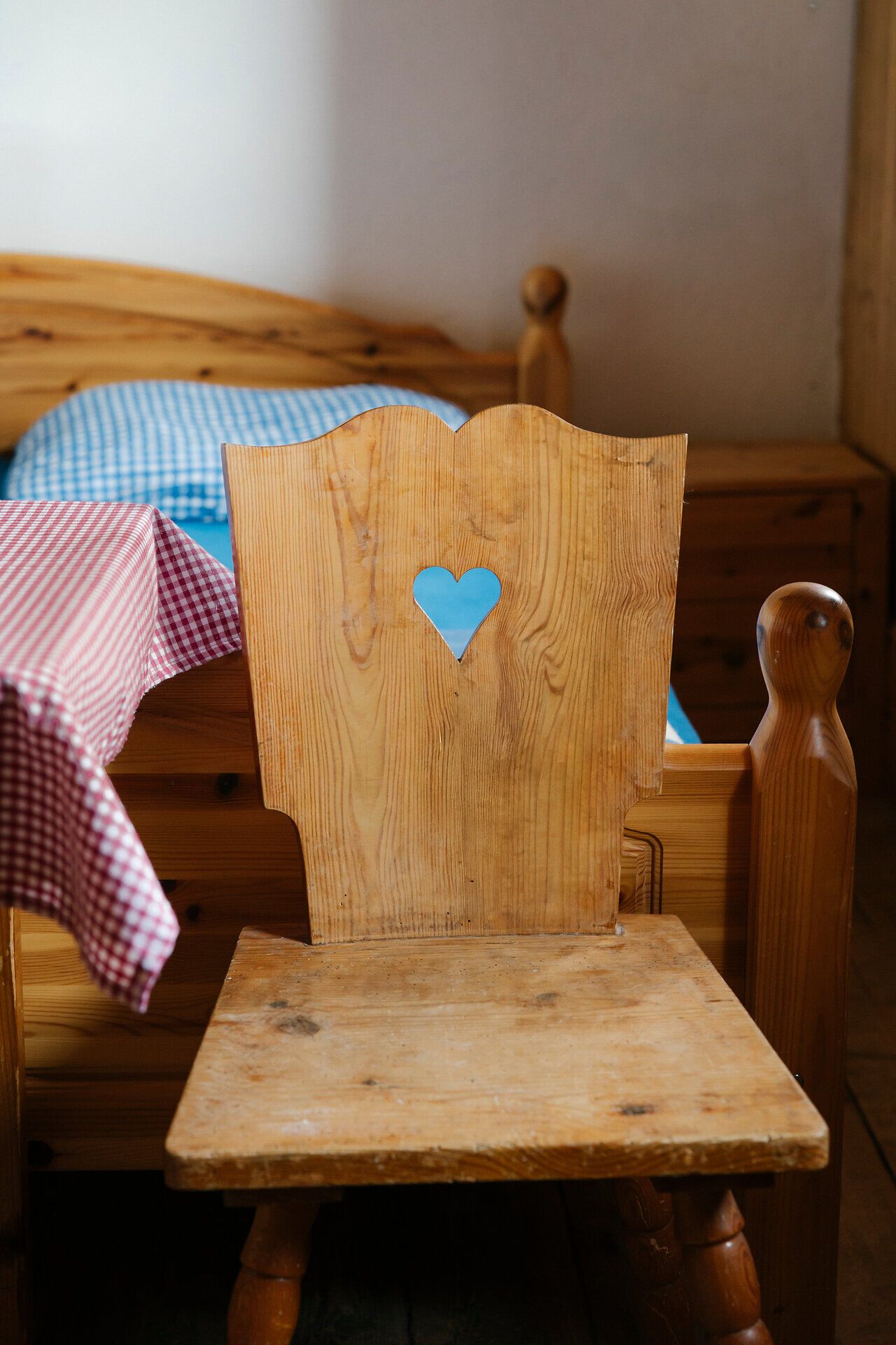 A rustic wooden chair with a heart-shaped cutout in front of a bed at the Edelweißhütte on Schneeberg